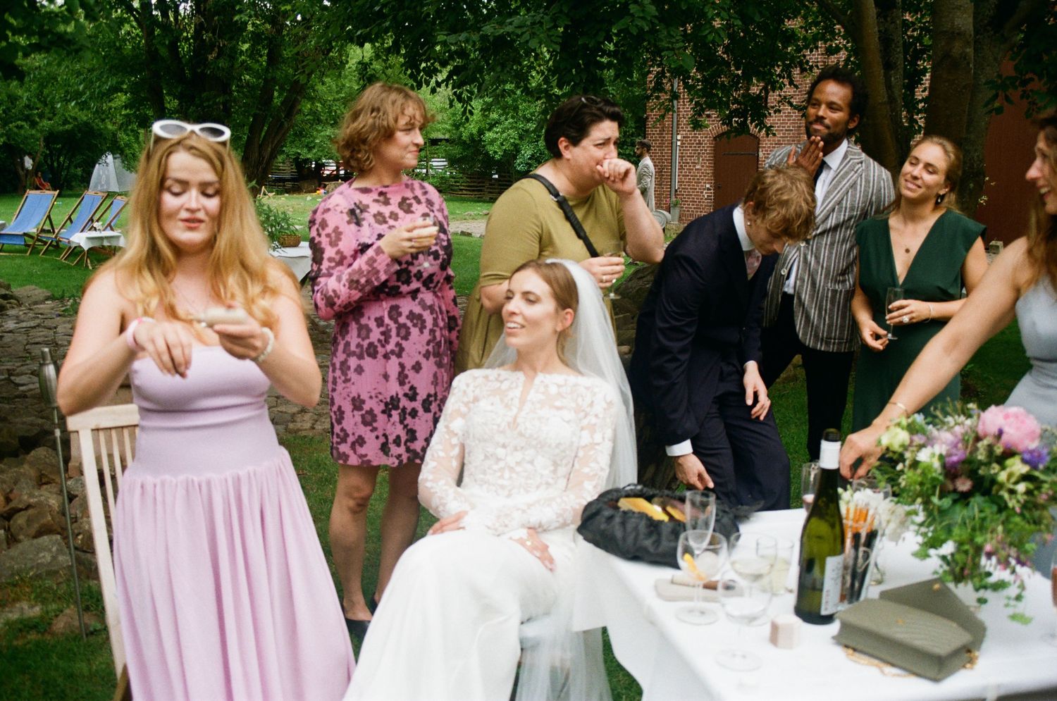 Wedding guests in pink bridesmaid dresses gather outdoors at a garden reception celebration.