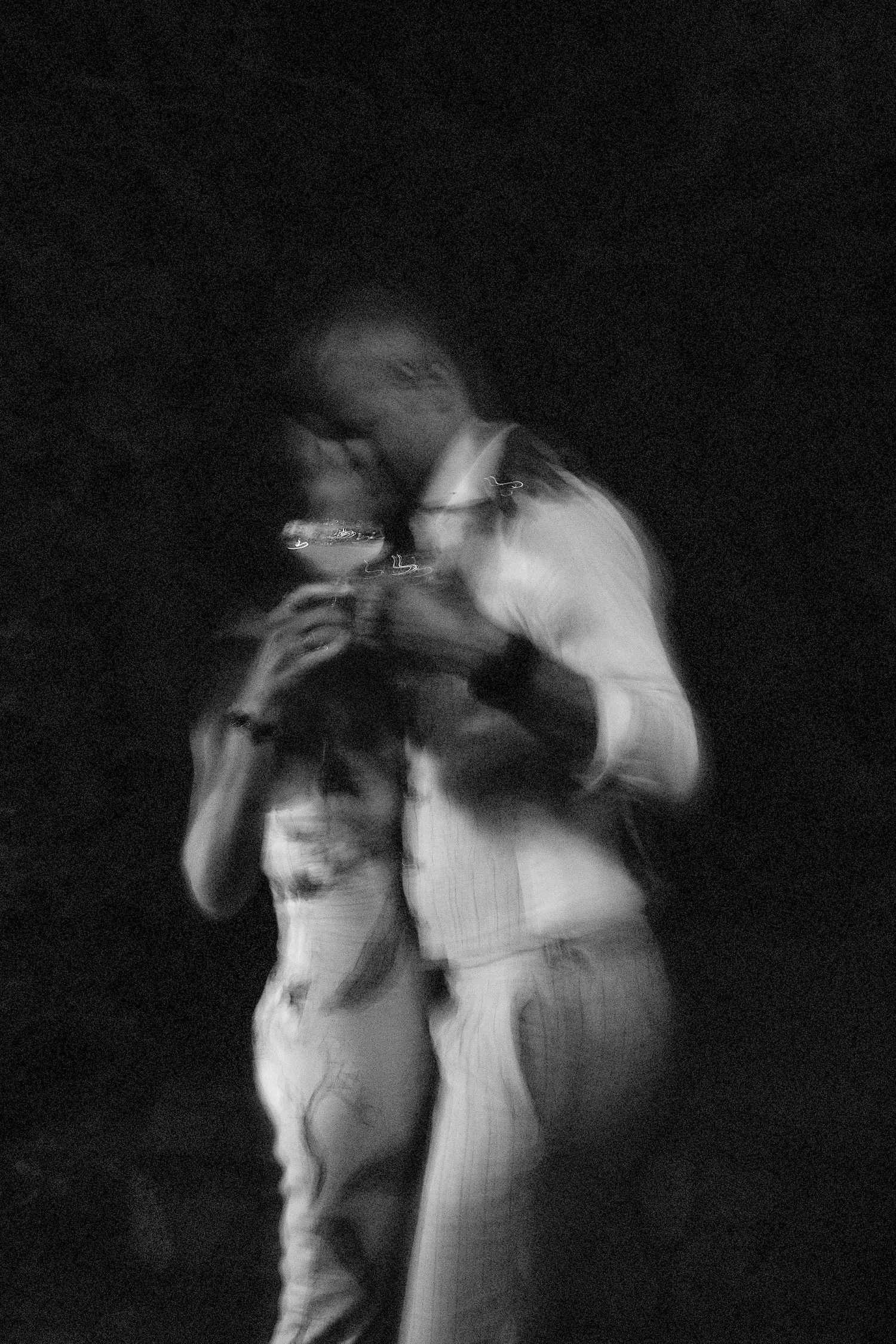 Blurry black and white photo of a couple embracing and kissing at night, motion blur creating dreamy effect.