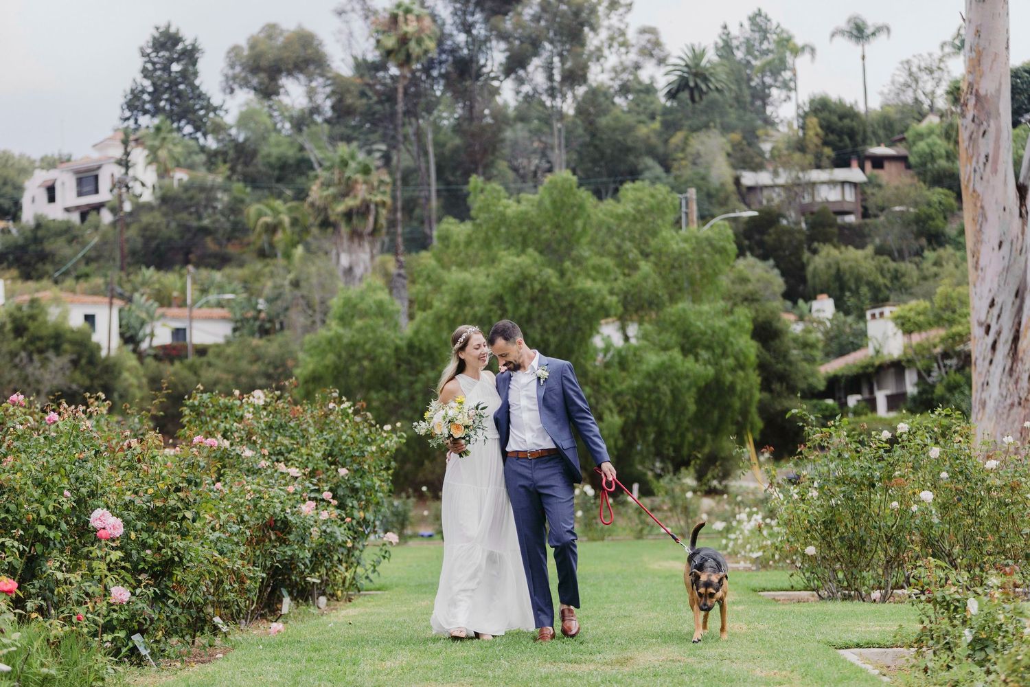 Couple walking through a lush garden path with trees and flowers at a wedding venue.