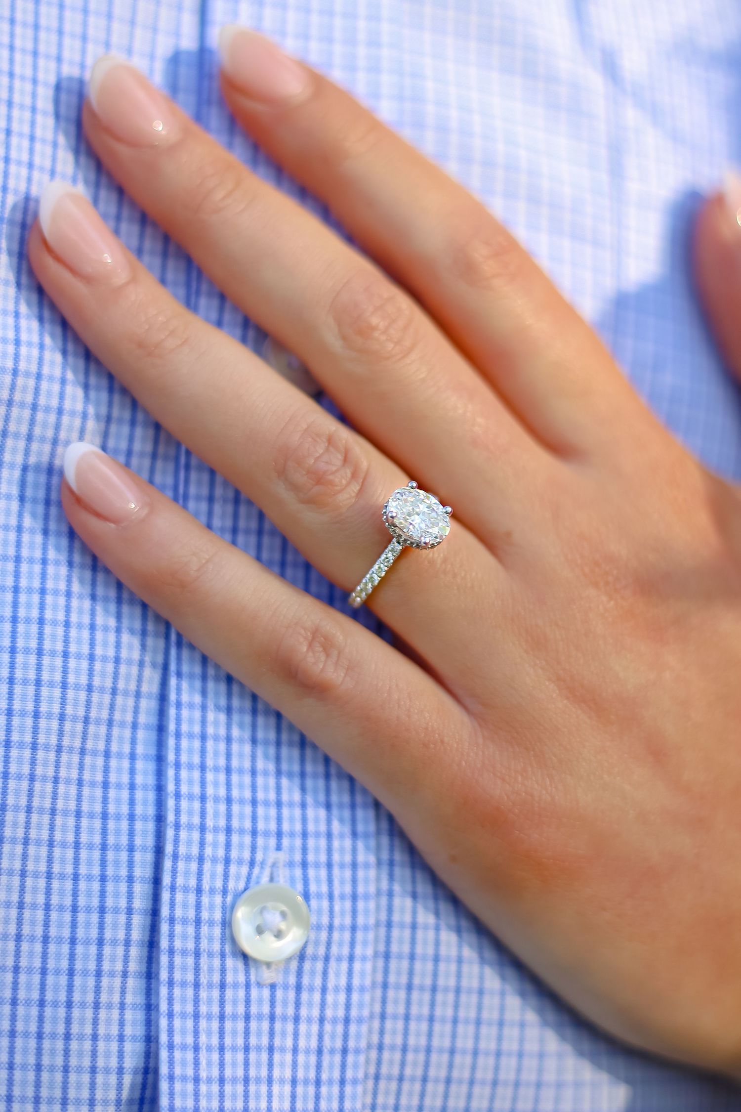 Close-up of a sparkling diamond engagement ring on a hand against a blue checkered shirt.