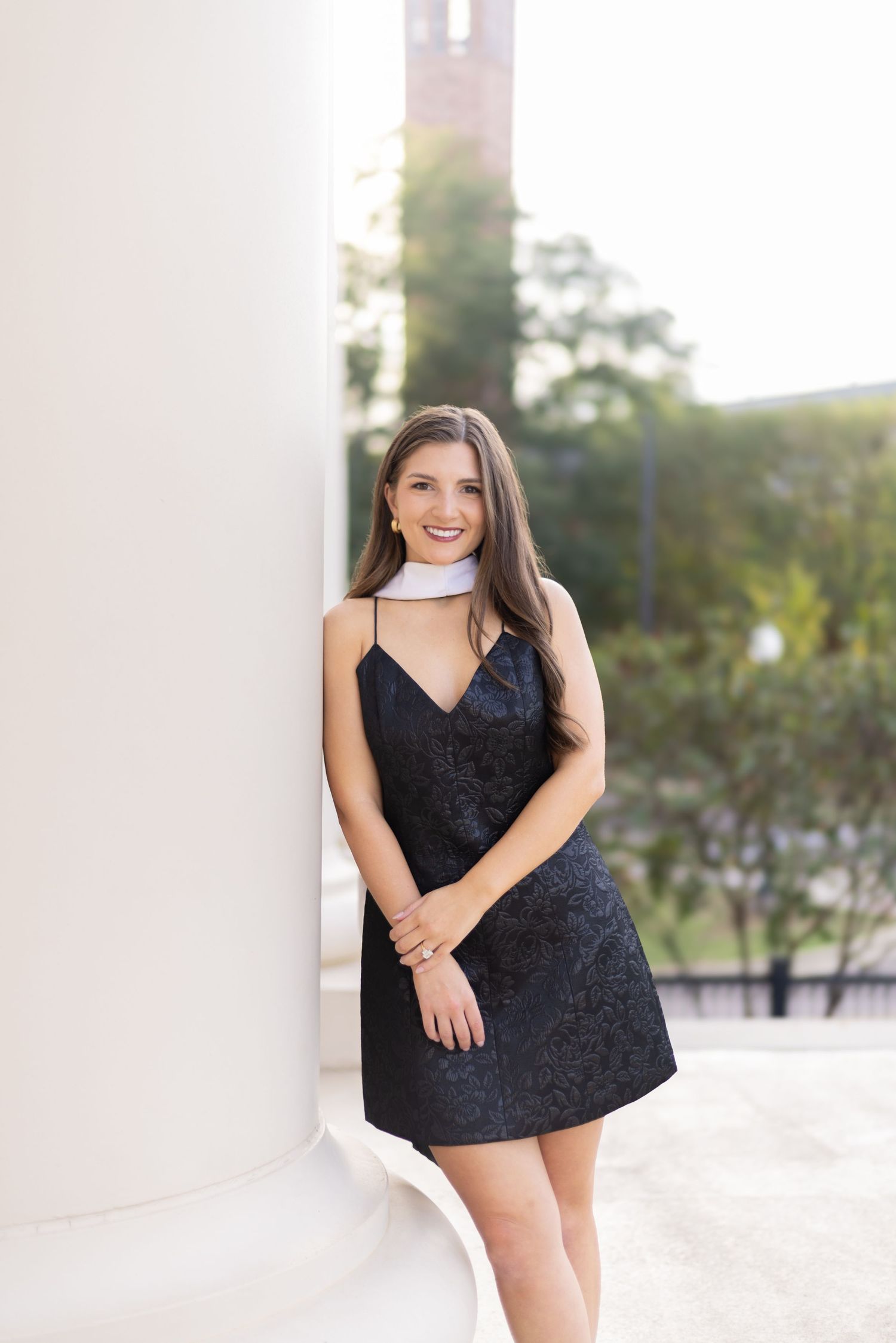 A person in a black dress poses against white columns during a photo session.