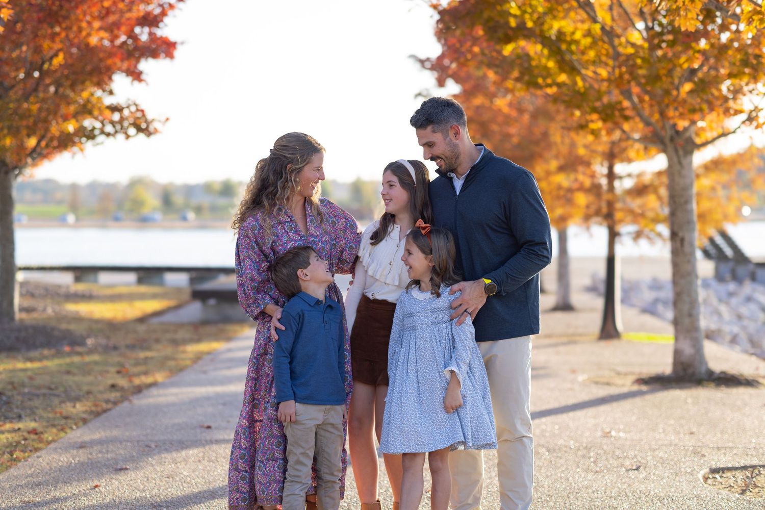 Family of five enjoying a fall outdoor portrait session with colorful autumn trees and waterfront backdrop.