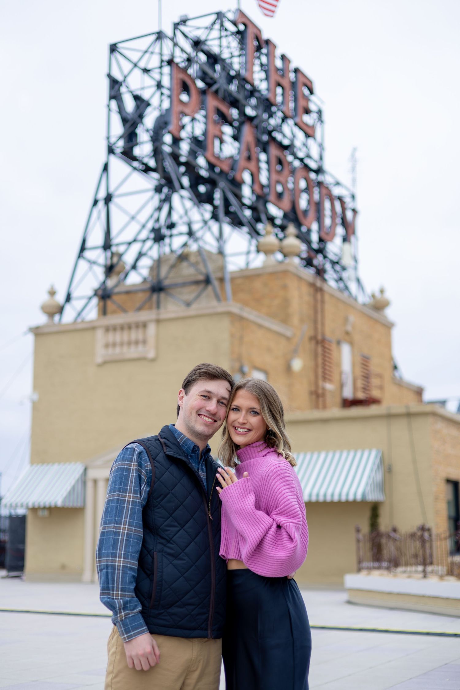 Couple smiling together in front of The Peabody hotel sign outdoors.