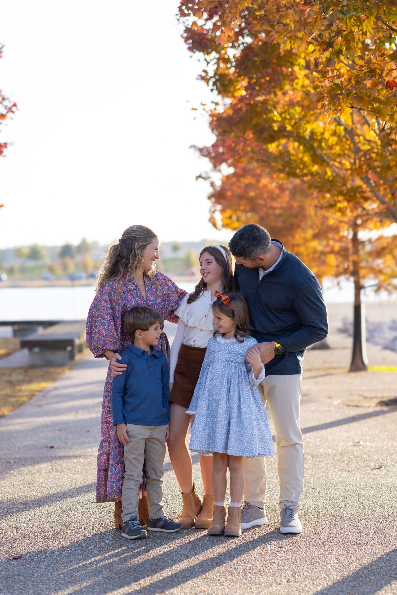 Family of five sharing a warm moment outdoors among vibrant autumn trees near a lake.