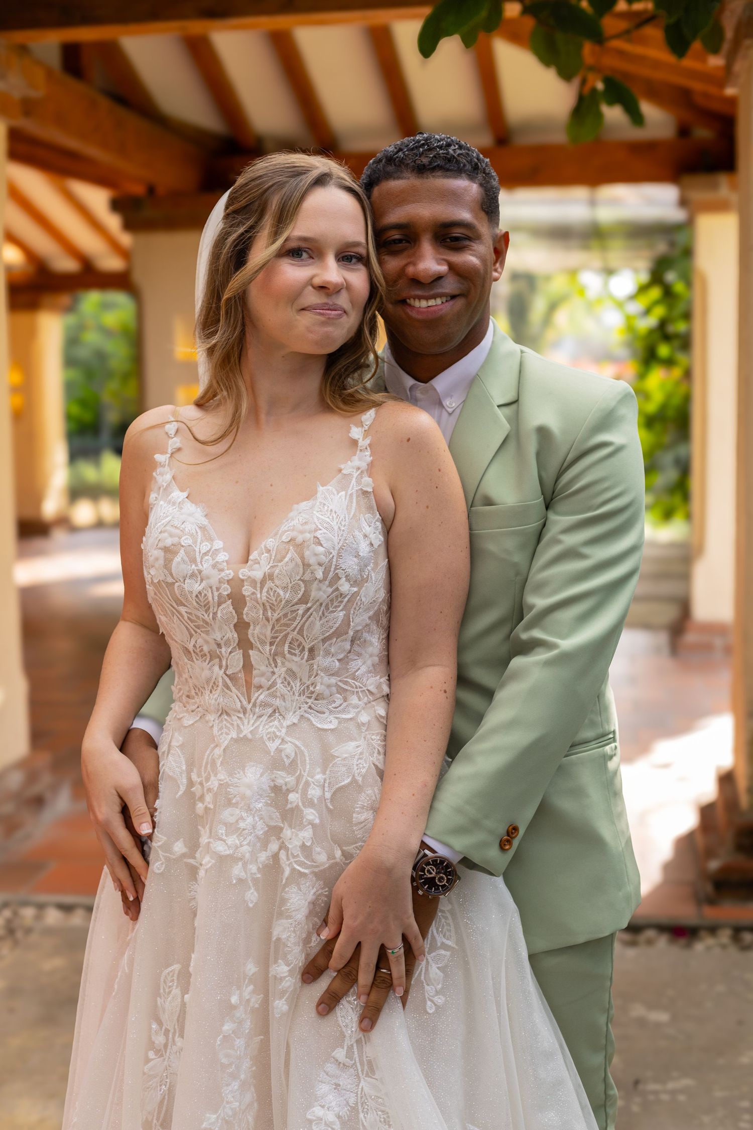 Wedding portrait of couple in mint green suit and lace gown under covered patio.