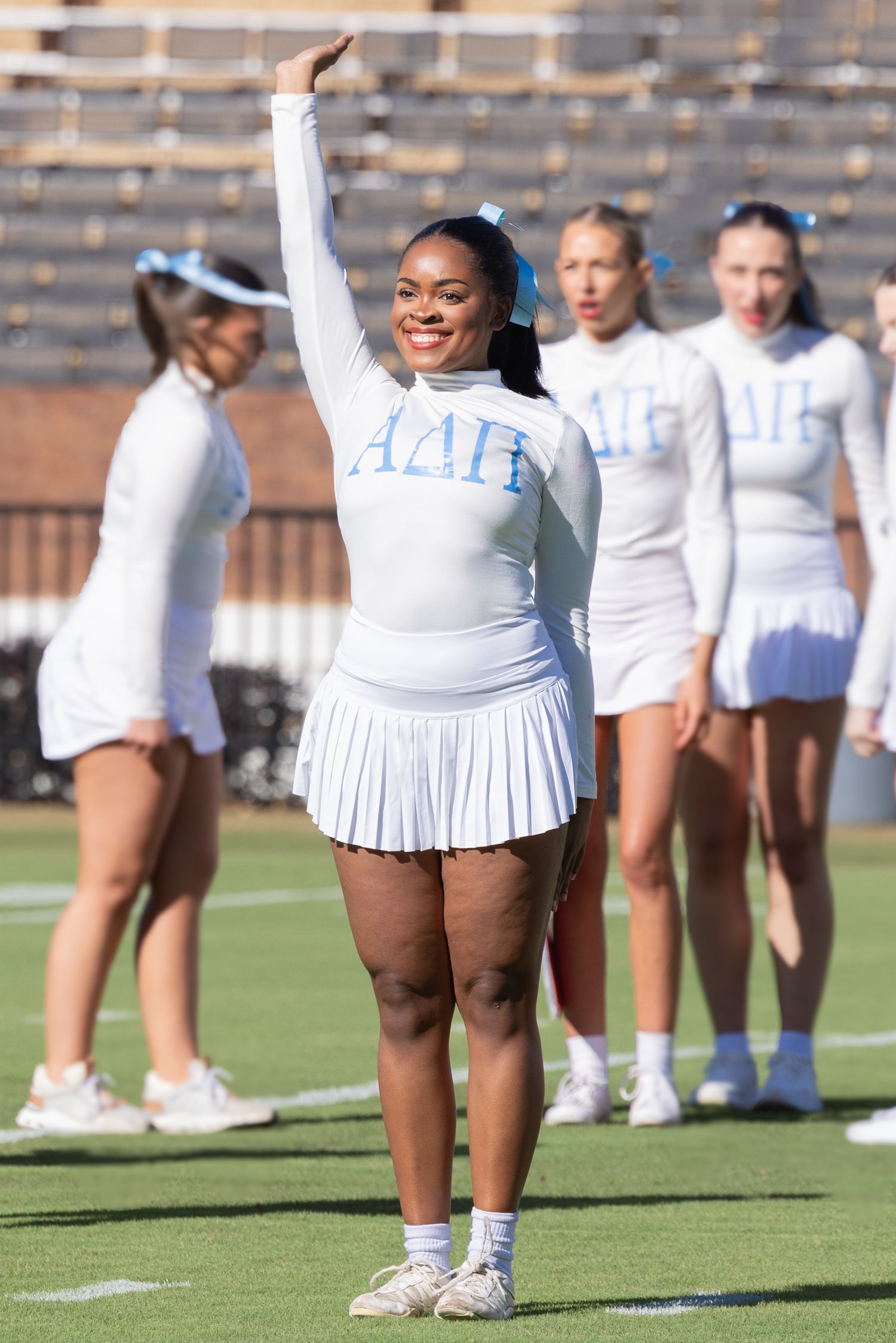 Cheerleaders in white uniforms practice routines on football field during daytime.