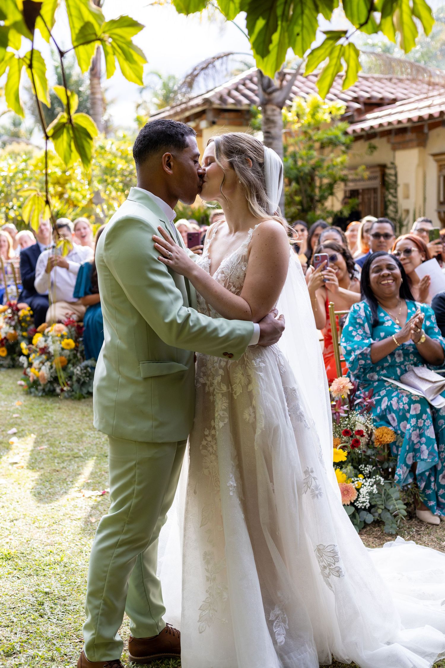 Bride and groom share their first kiss during an outdoor garden wedding ceremony as guests look on and celebrate.