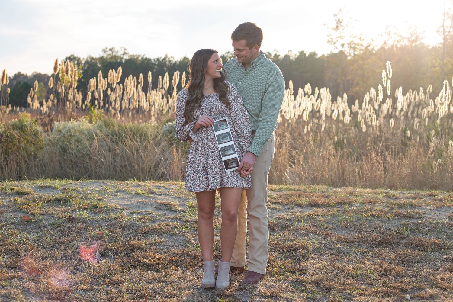 Couple poses together at sunset in field with tall grass and golden lighting.
