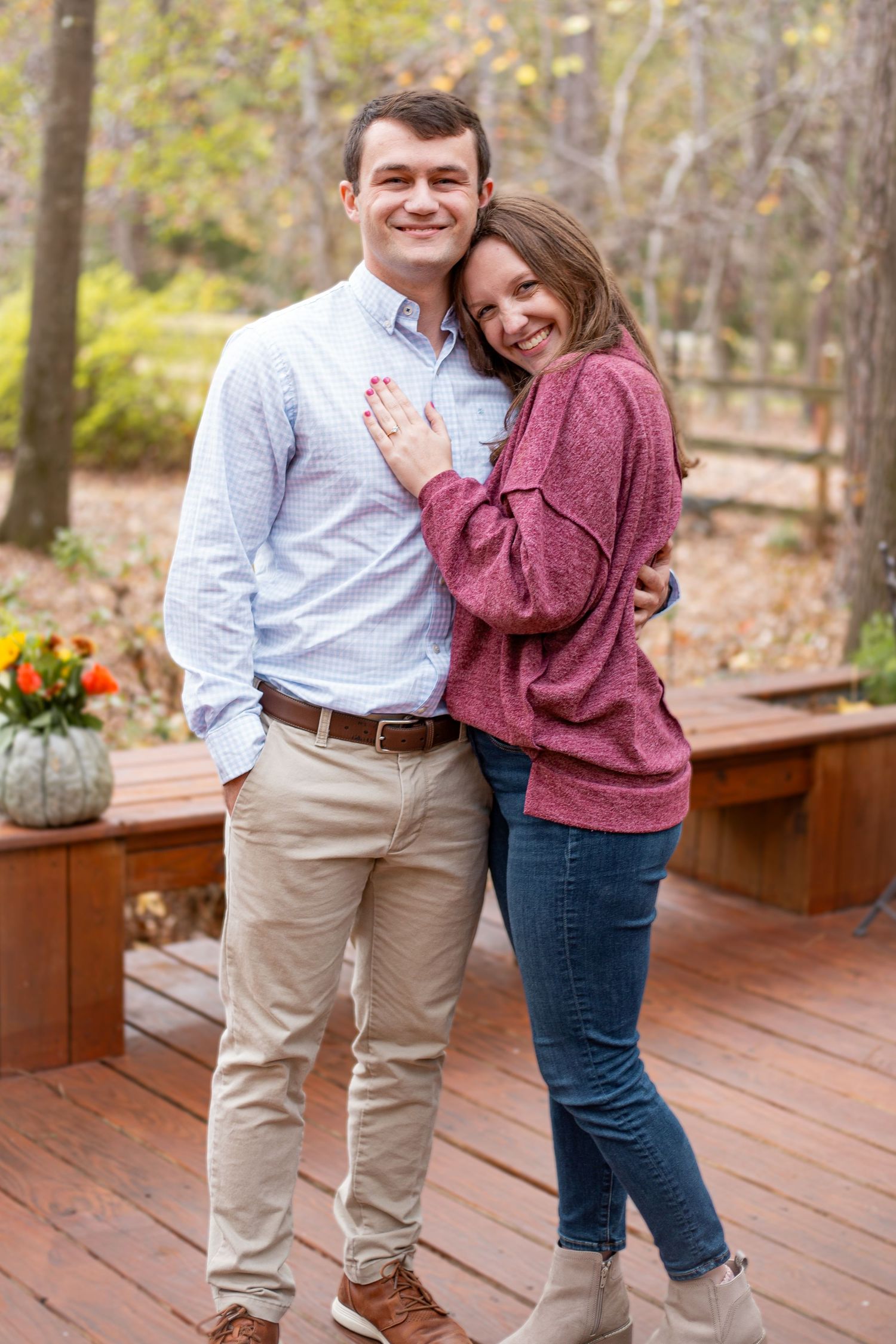 A happy couple celebrates their engagement on a wooden deck with fall decorations.