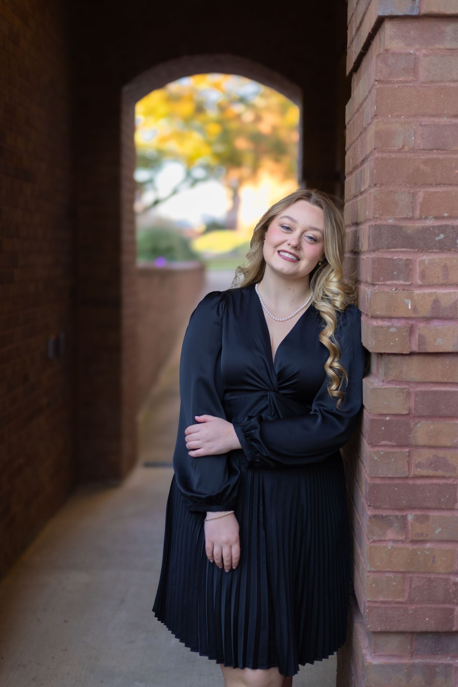 Portrait session against brick wall backdrop with natural lighting and fall colors.