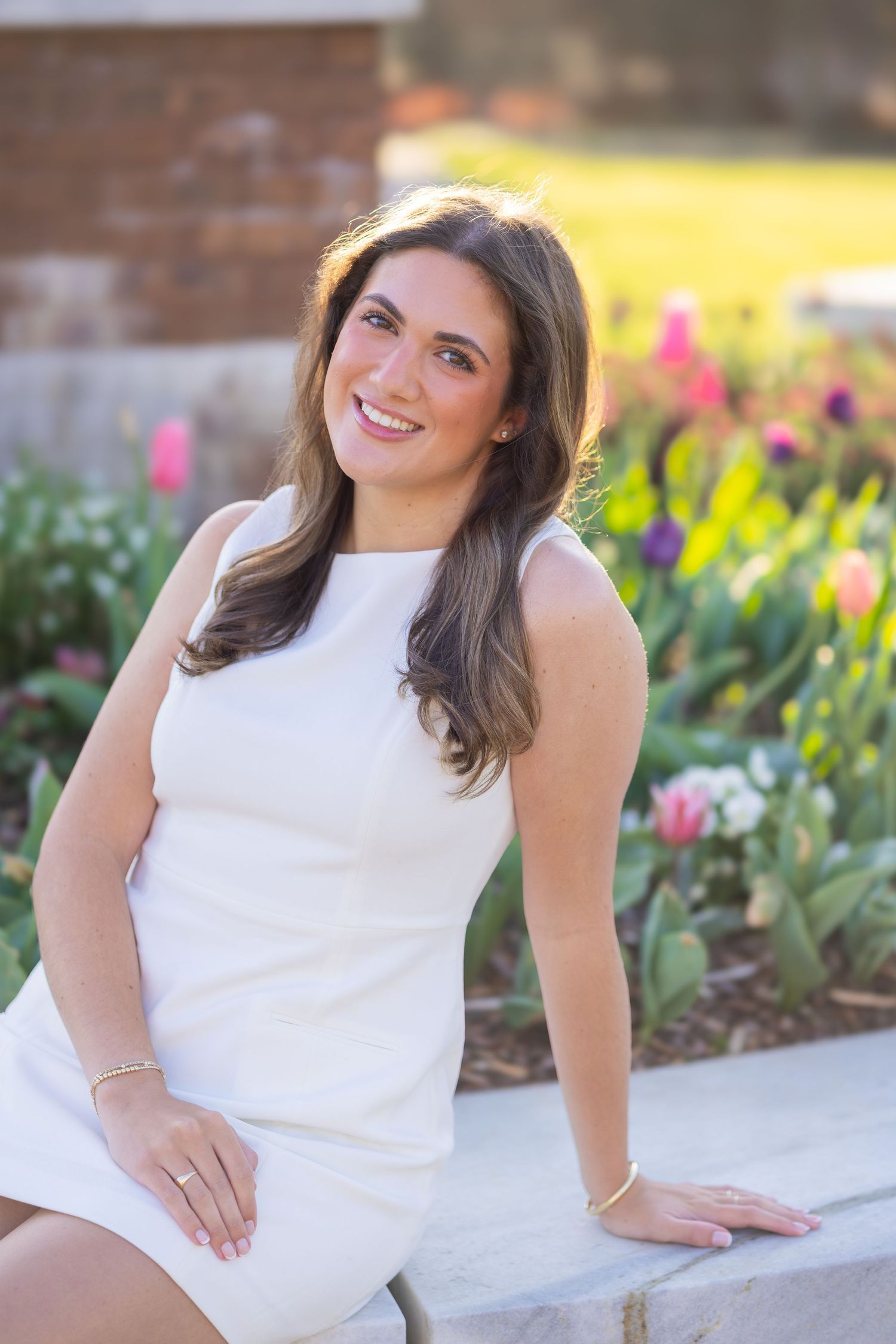 Young woman in white dress smiling outdoors among colorful tulips in bloom during springtime.