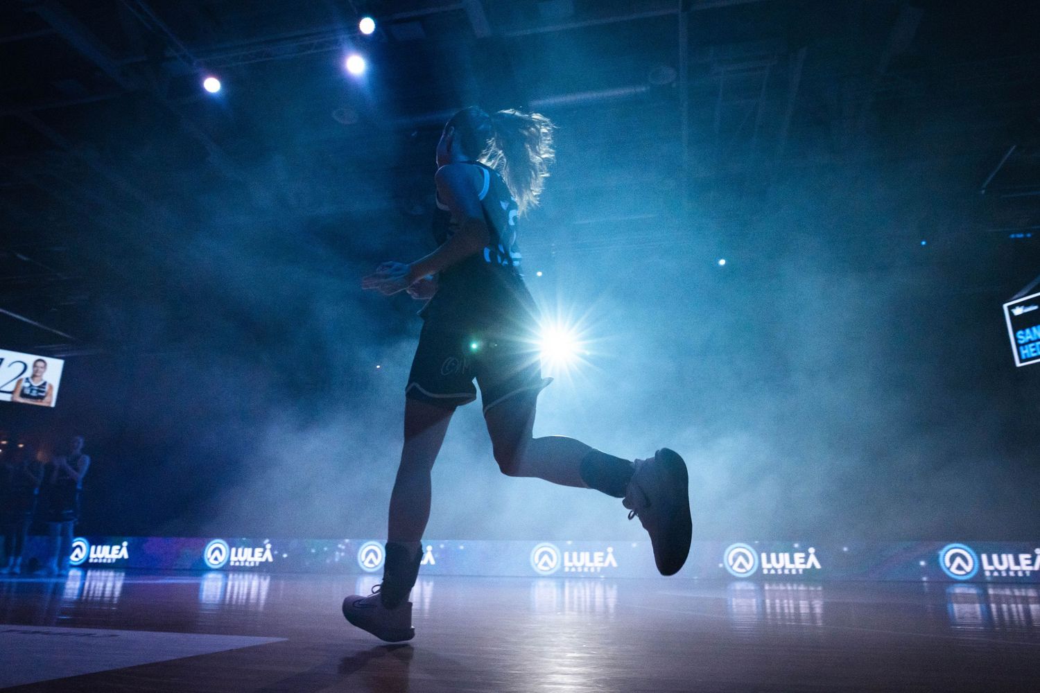 Figure skater performs on dark ice rink with dramatic blue lighting and fog effects creating moody atmosphere.