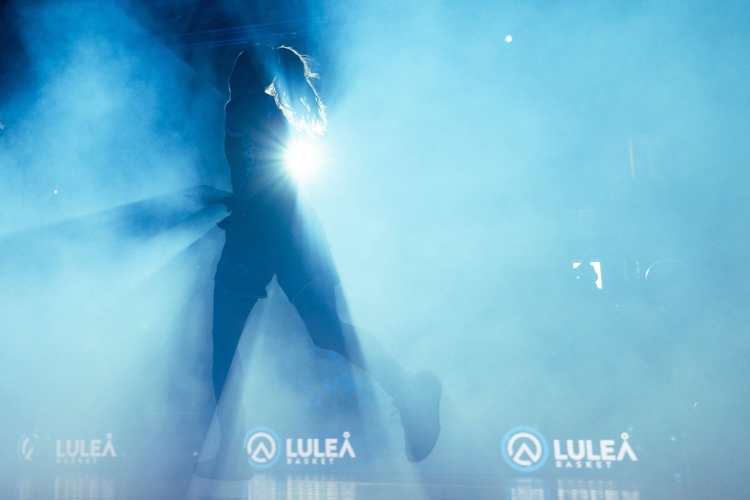 Silhouetted performer on stage surrounded by blue smoke and bright spotlight at Luleå Arena event.