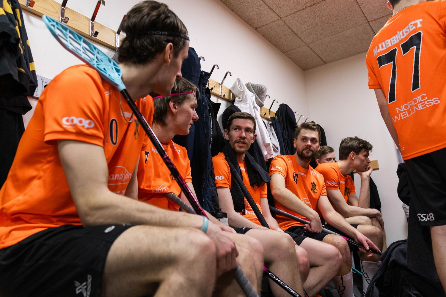 Players in orange jerseys huddle together in a locker room during a team meeting.