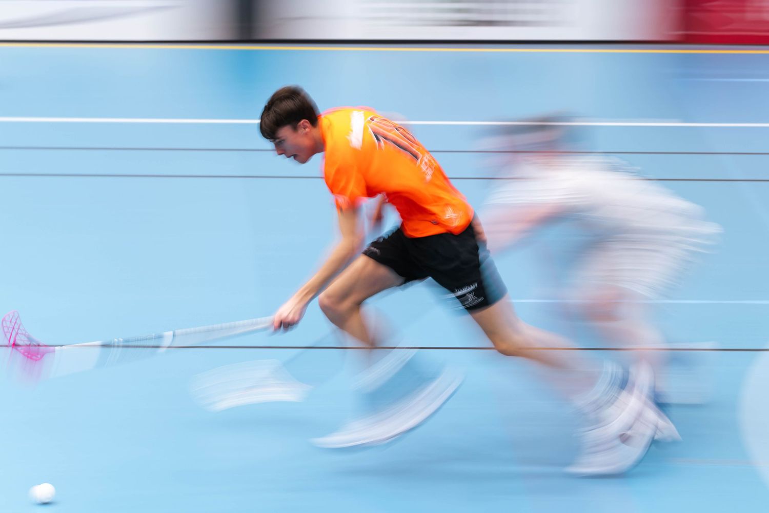 A sequence of motion-blurred shots showing a speed skater gliding across an indoor ice rink in an orange uniform.