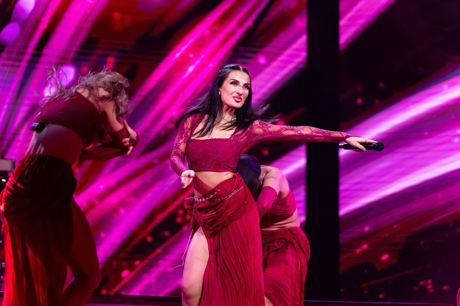 Performer in red dress sings on stage with dramatic pink and purple lighting effects during live concert performance.
