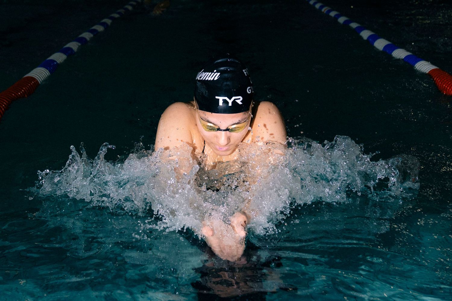 Competitive swimmer performing breaststroke in an indoor pool wearing a TYR swim cap during a race.