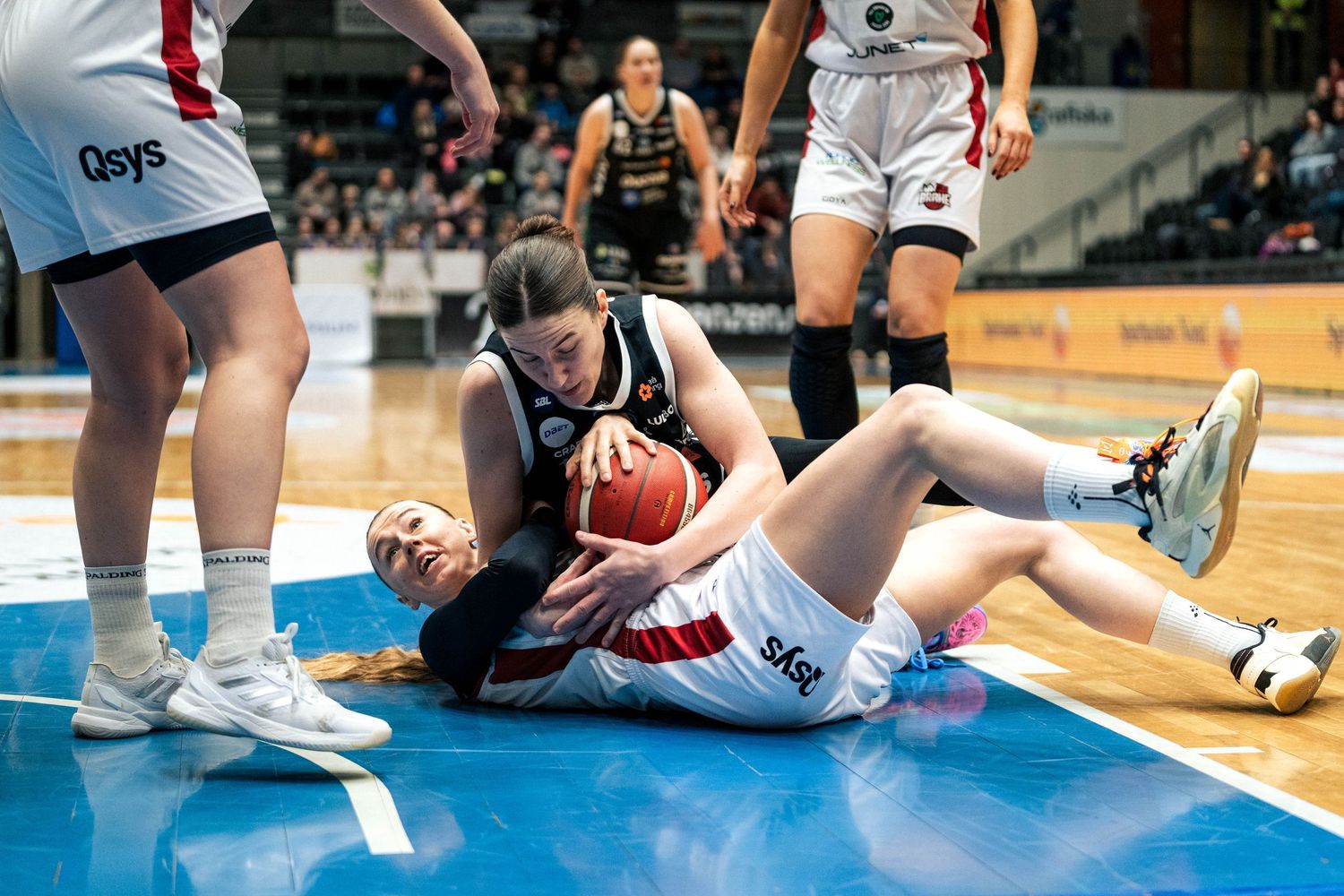 Athletes in white and red uniforms compete for possession of the ball during an indoor volleyball match.