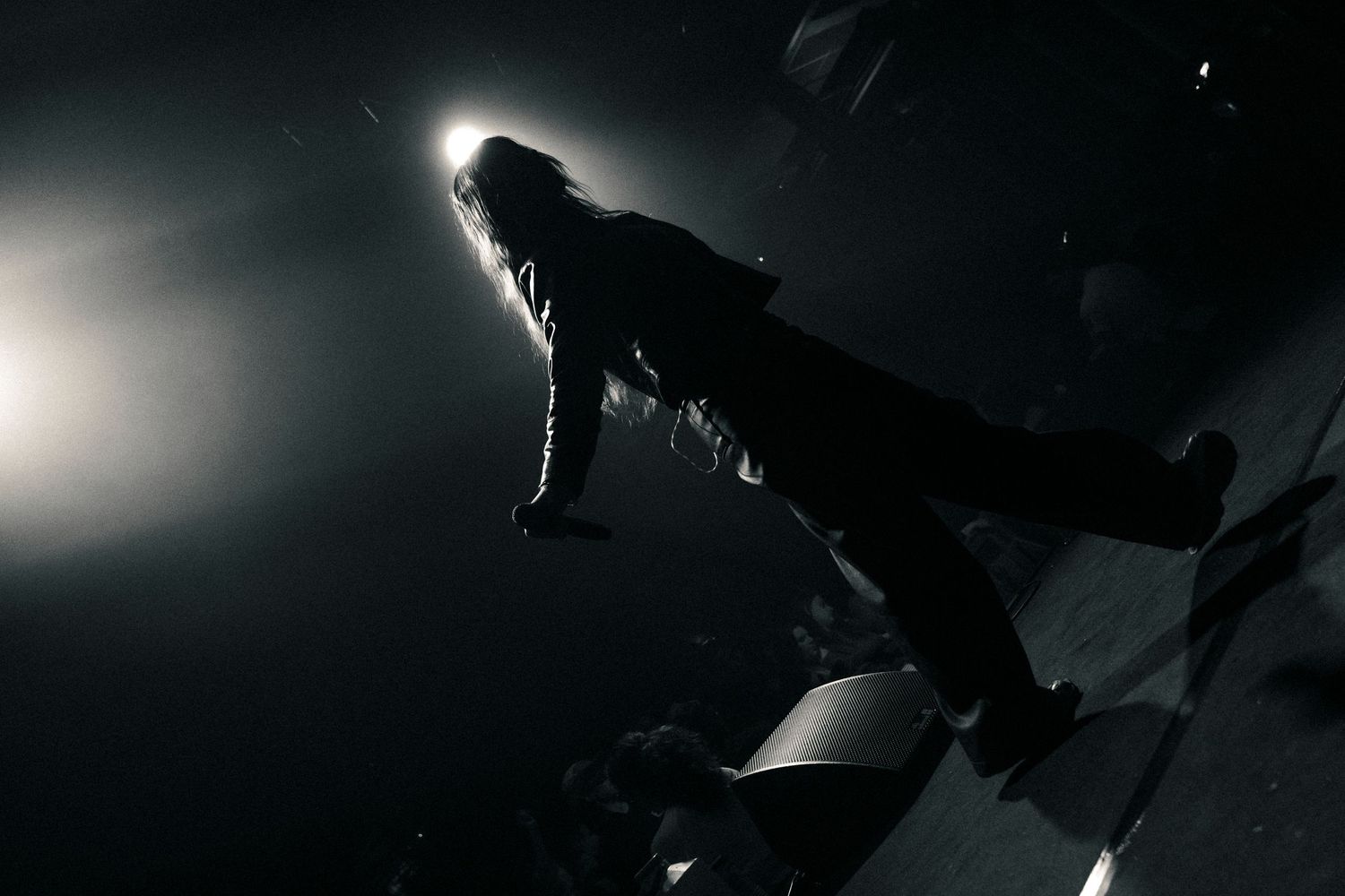 Silhouetted performer on stage under dramatic spotlight in dark concert venue.