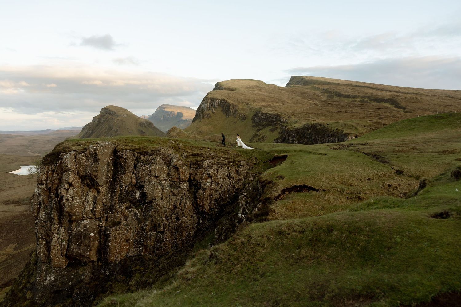 Dramatic Scottish Highlands landscape featuring rugged green cliffs and misty mountain peaks under a cloudy sky.
