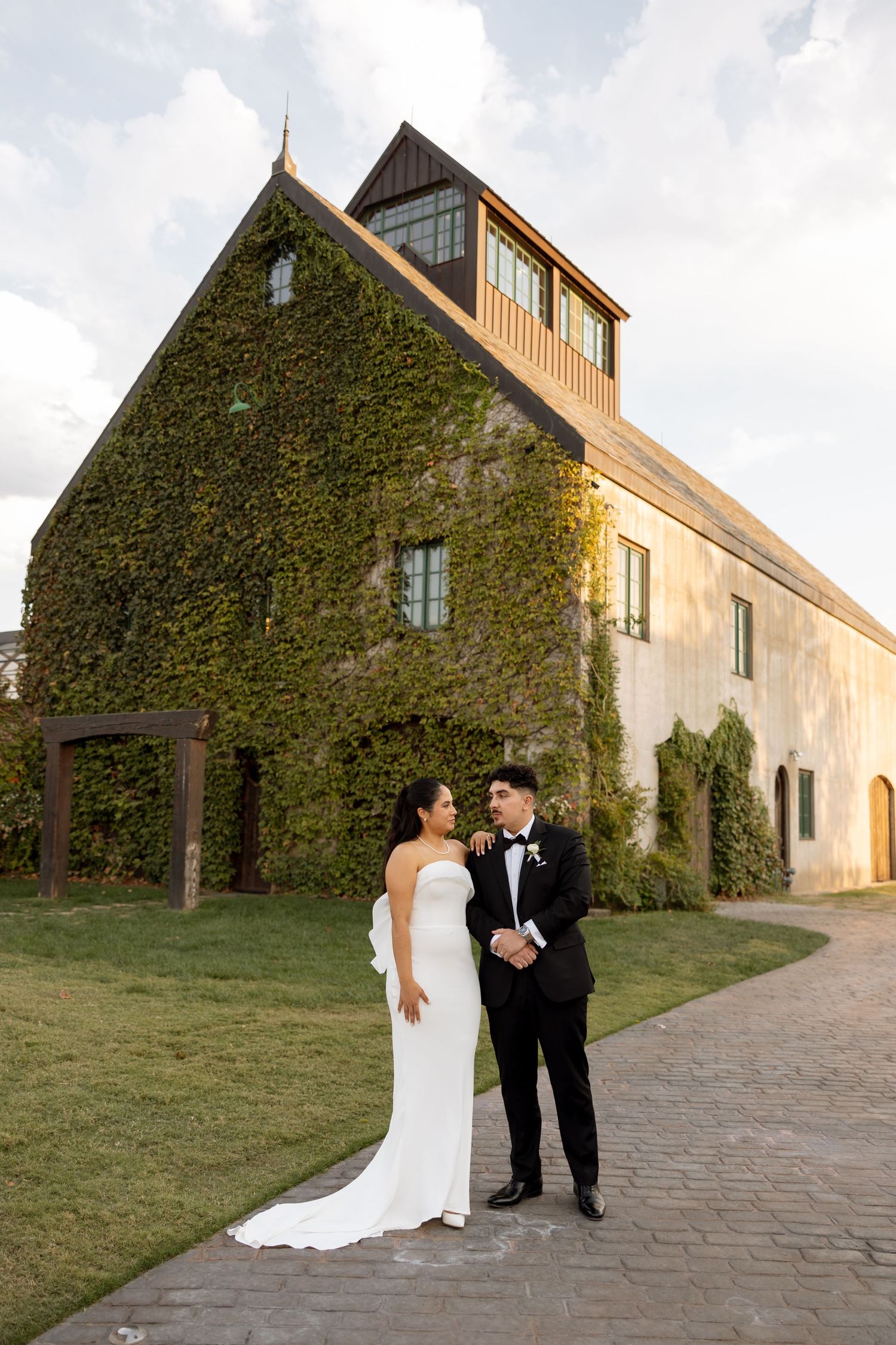 Newlyweds pose in formal attire against an ivy-covered stone building.