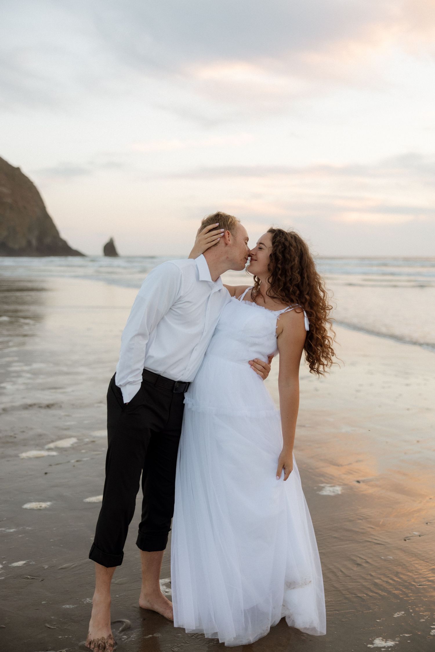Romantic beach wedding portrait at sunset with coastal cliffs in background.