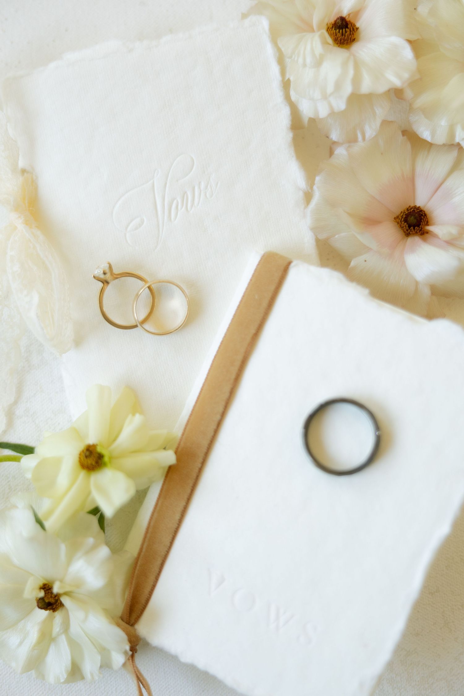 Wedding vow books with gold and black rings, white flowers, and embossed text on handmade paper.