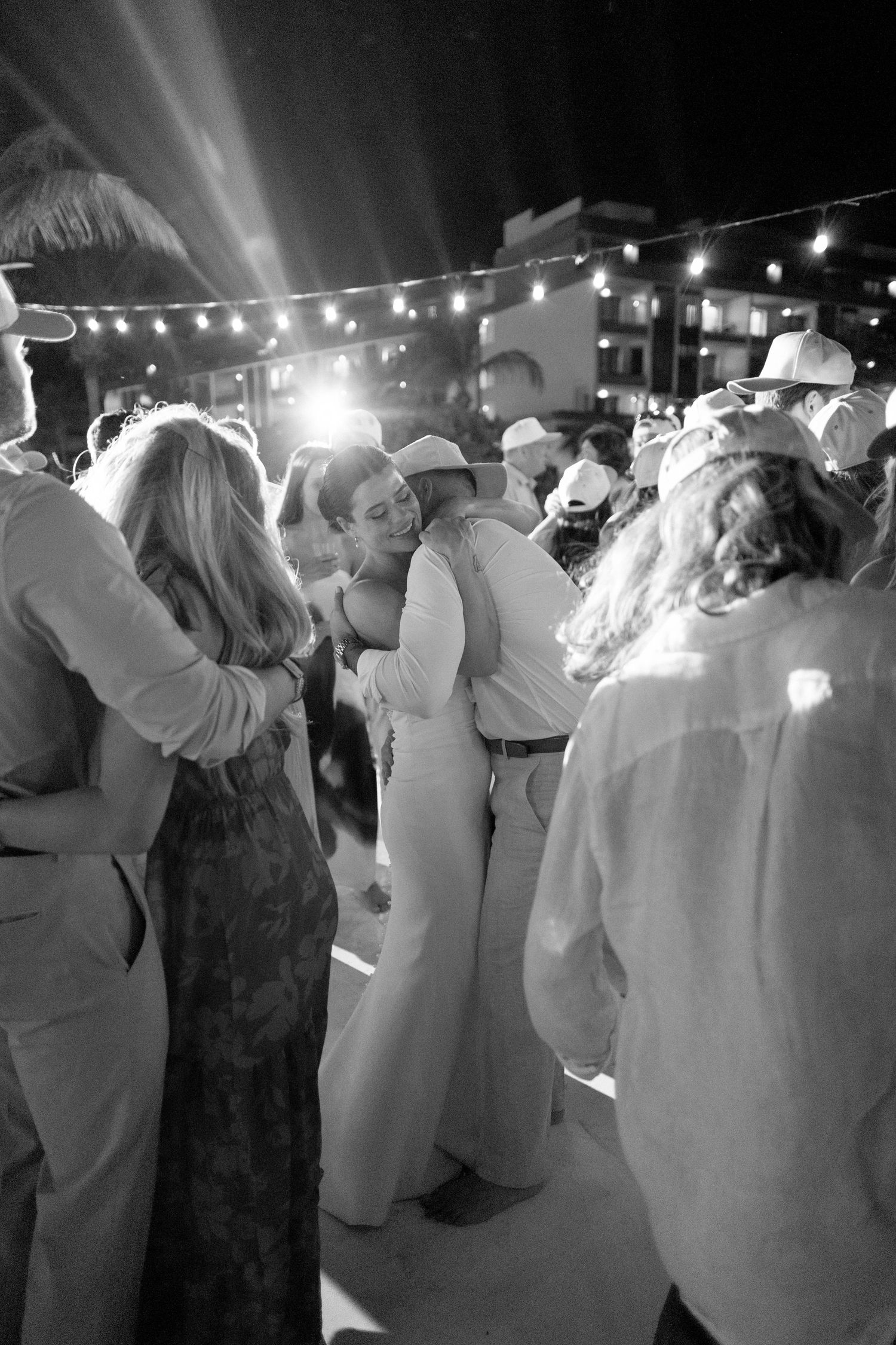 Black and white photo of guests dancing outdoors at a night wedding reception with string lights glowing above.