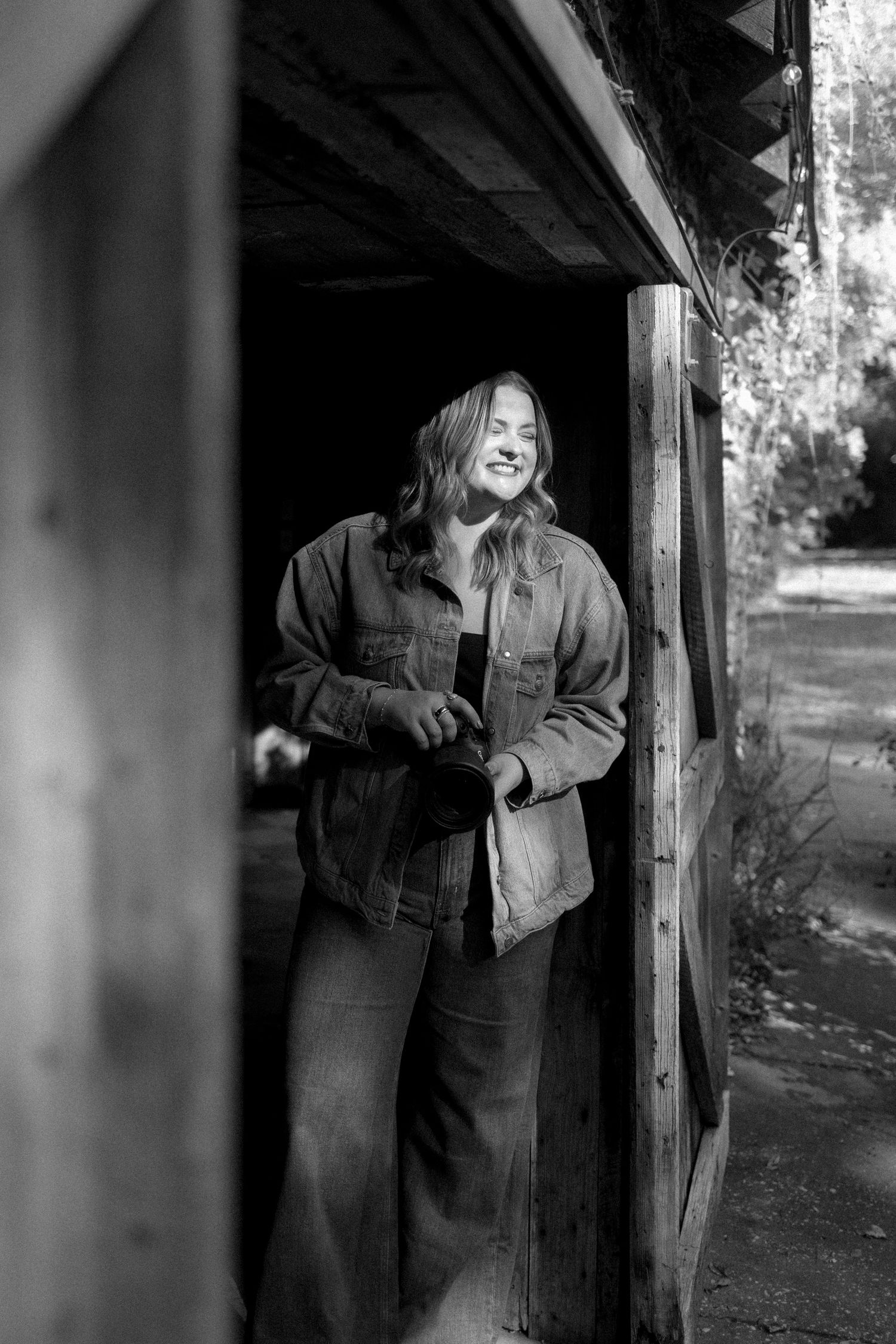 A person stands in a shadowy doorway wearing a denim jacket, creating a moody black and white portrait.