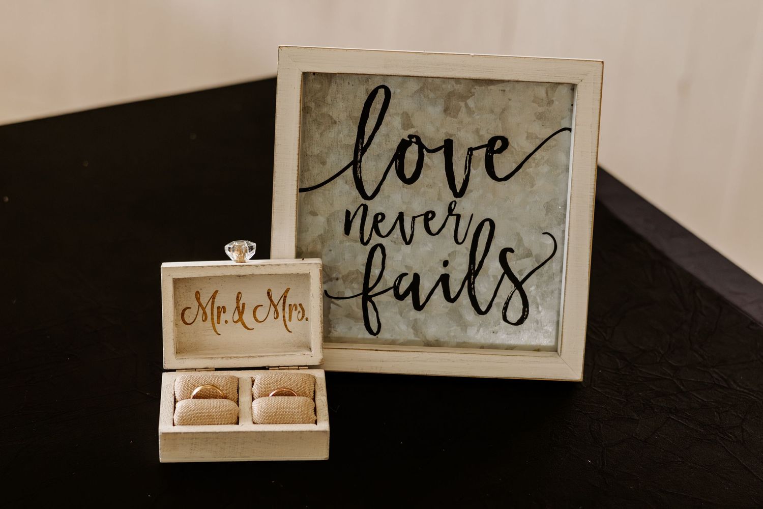 Wooden Mr. & Mrs. wedding ring box holding two rings beside a framed 