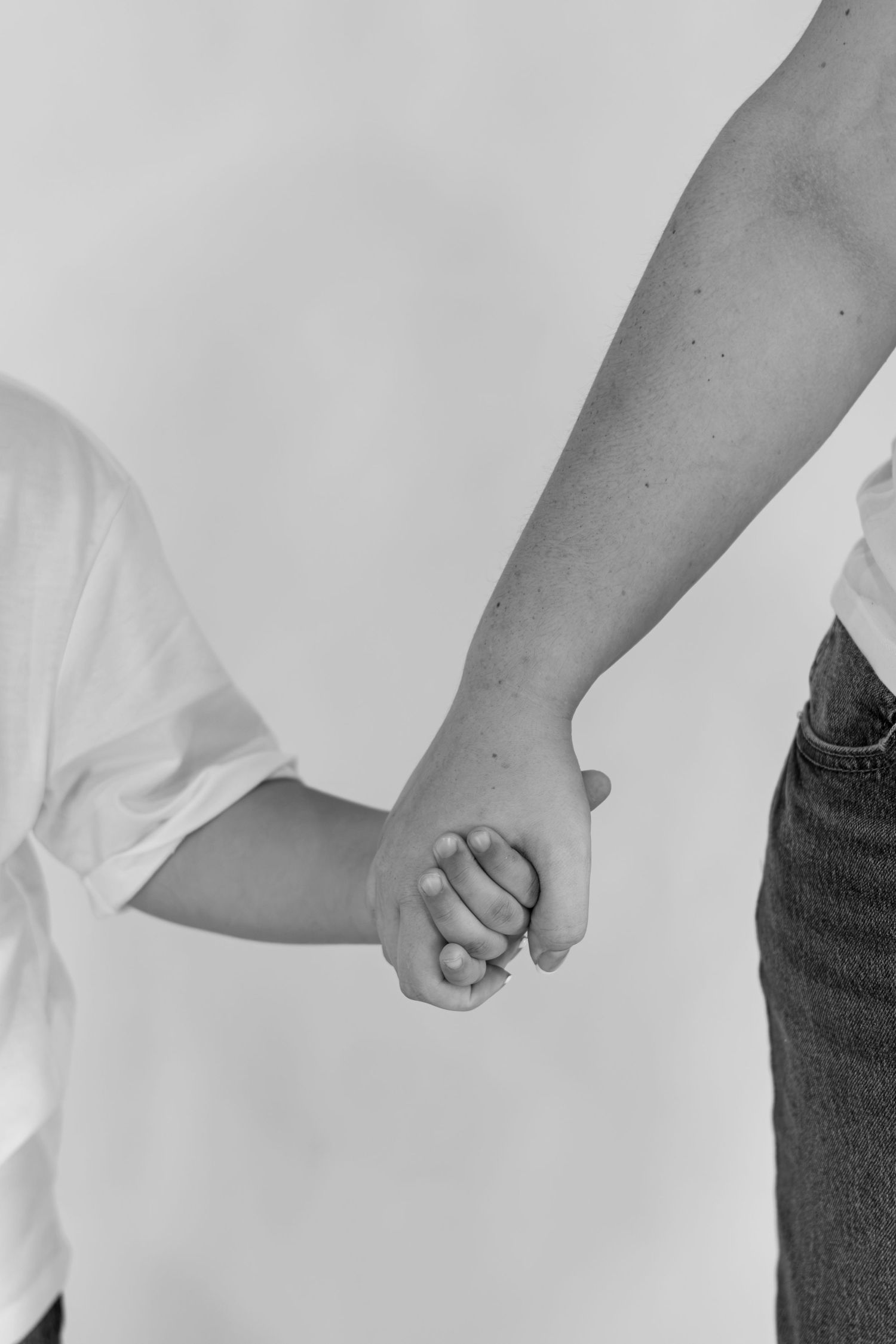 Black and white close-up of an adult and child holding hands against a plain light background.