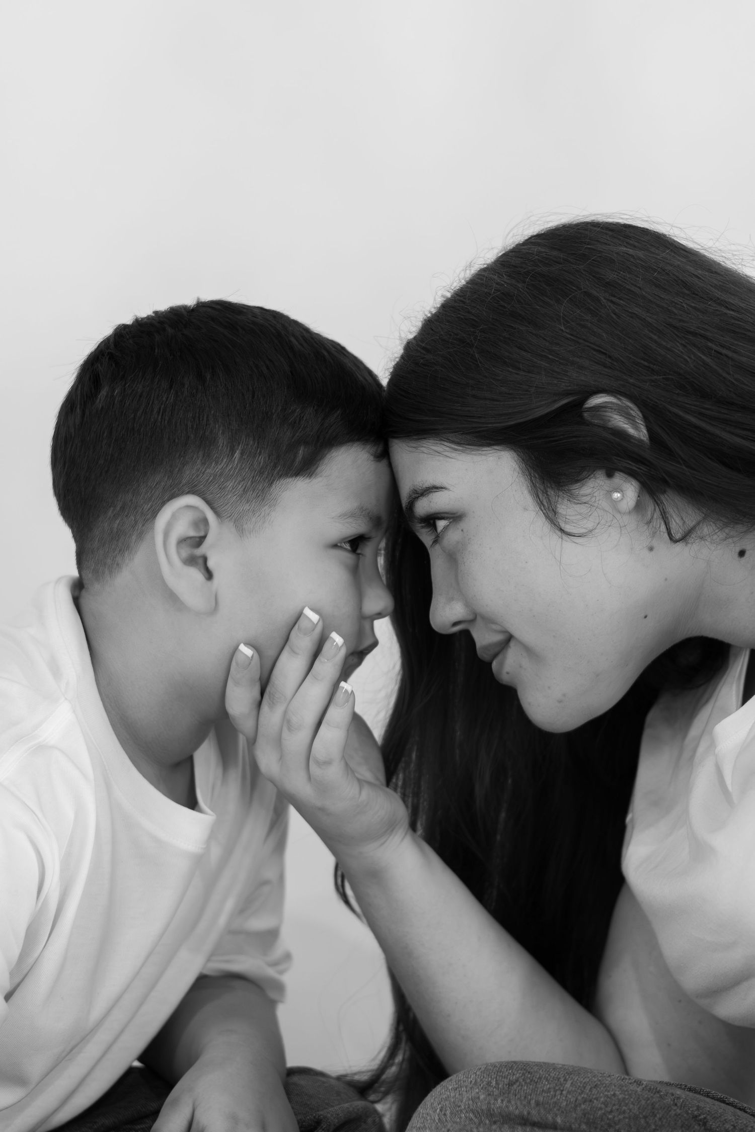 Black and white portrait of a mother and young son touching foreheads as she gently cups his cheek.
