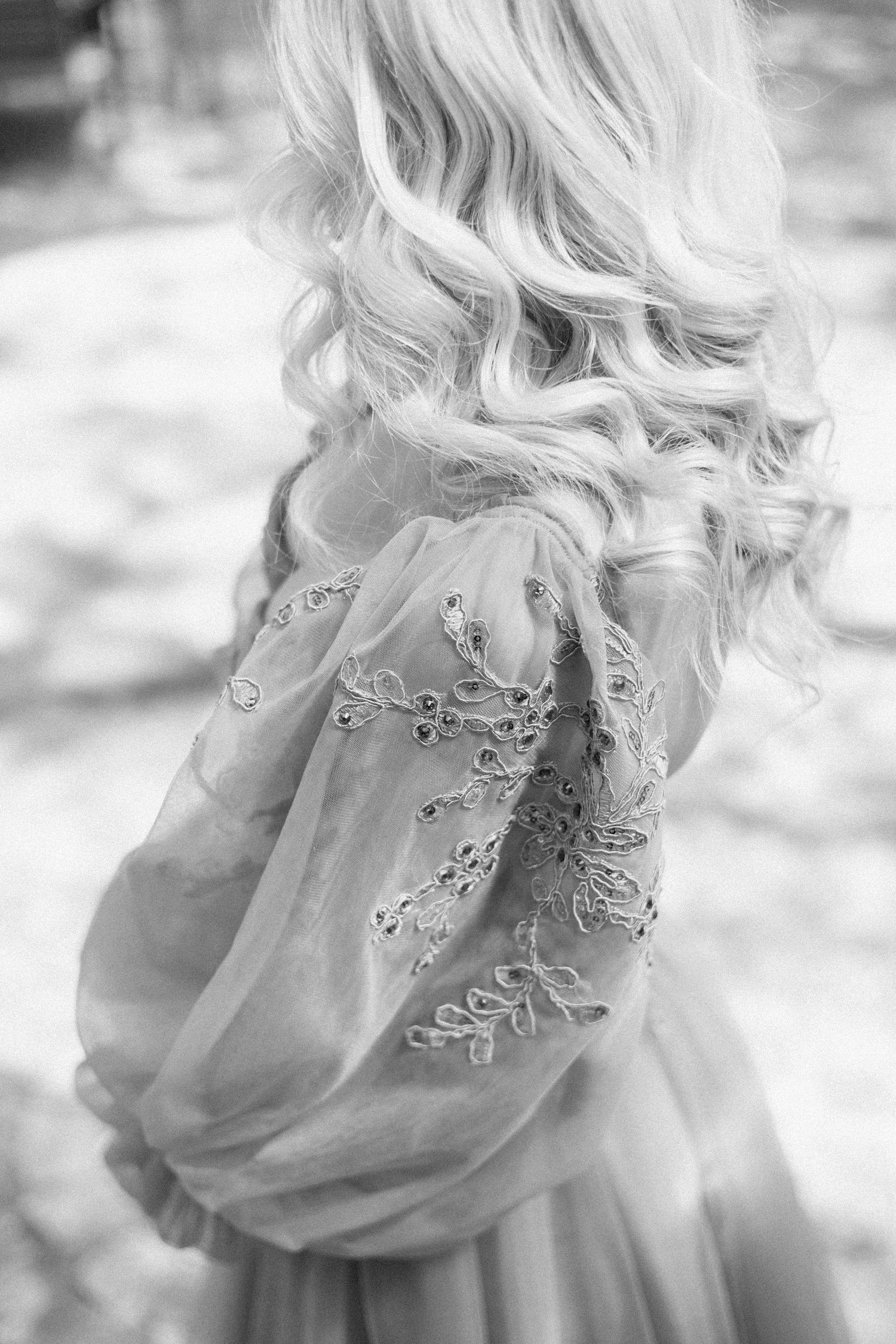 Black and white photo of a woman with long wavy blonde hair wearing a dress with embroidered sheer puffed sleeves.