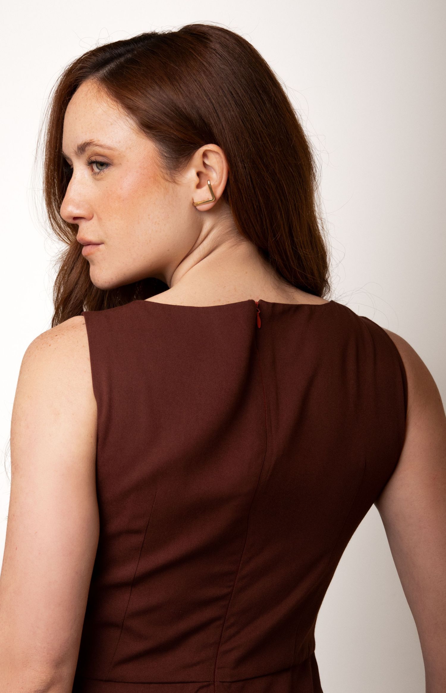 Close-up back view of a brown sleeveless dress with a red zipper detail and seamed bodice, worn by a woman with long auburn hair.