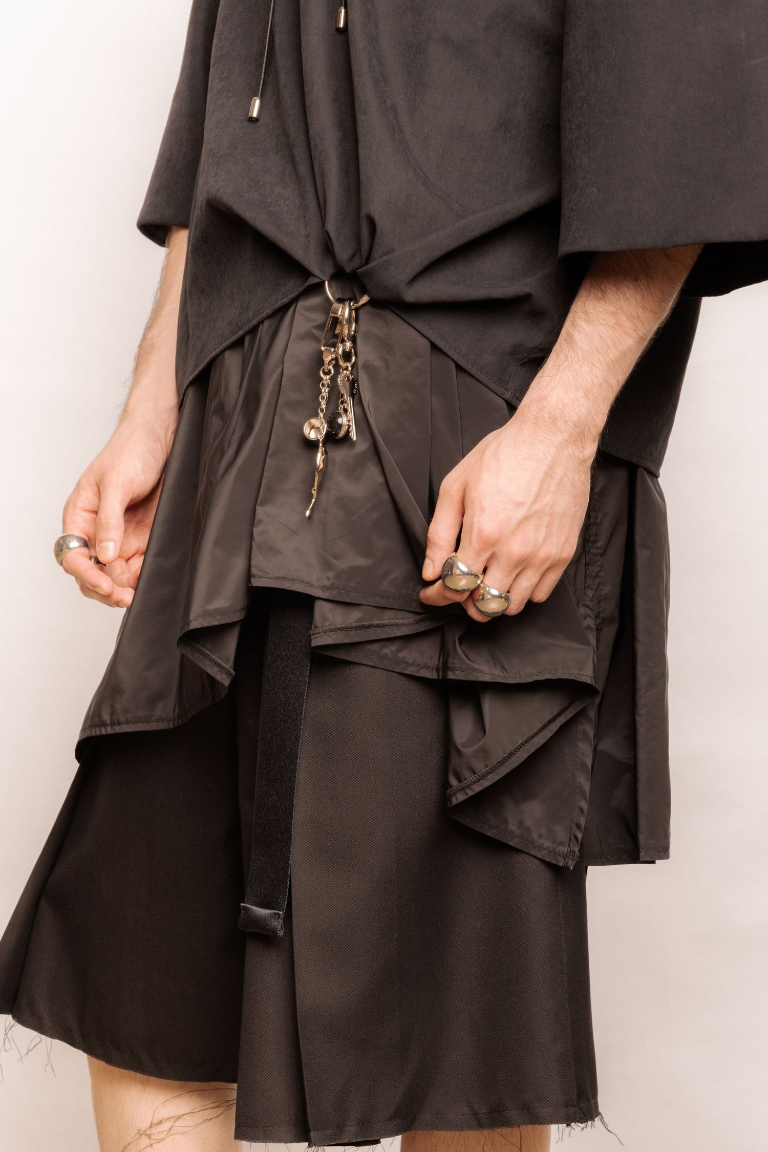Close-up of layered black asymmetric shorts and a draped top with silver charm keychain and chunky silver rings.