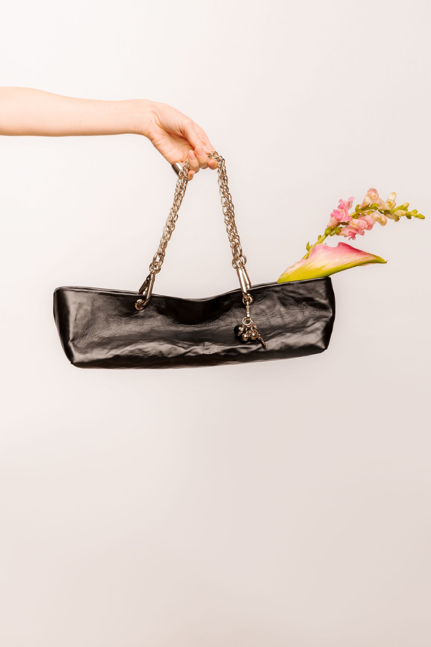 Hand holding a black crinkled leather baguette handbag with a chunky silver chain strap and a pink flower tucked inside.