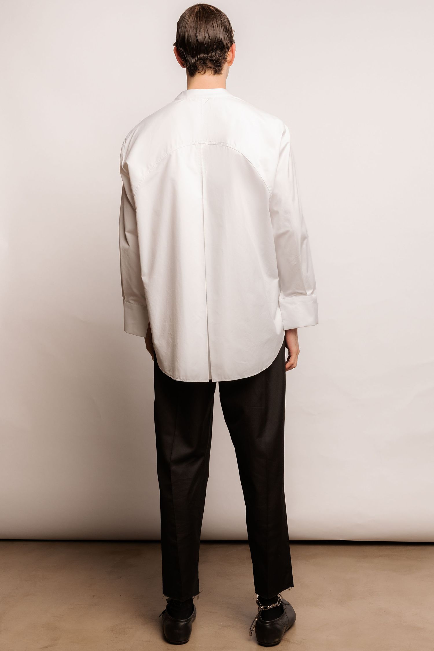 Back view of a model in an oversized white shirt with cuffed sleeves, black tapered trousers and black lace-up shoes.