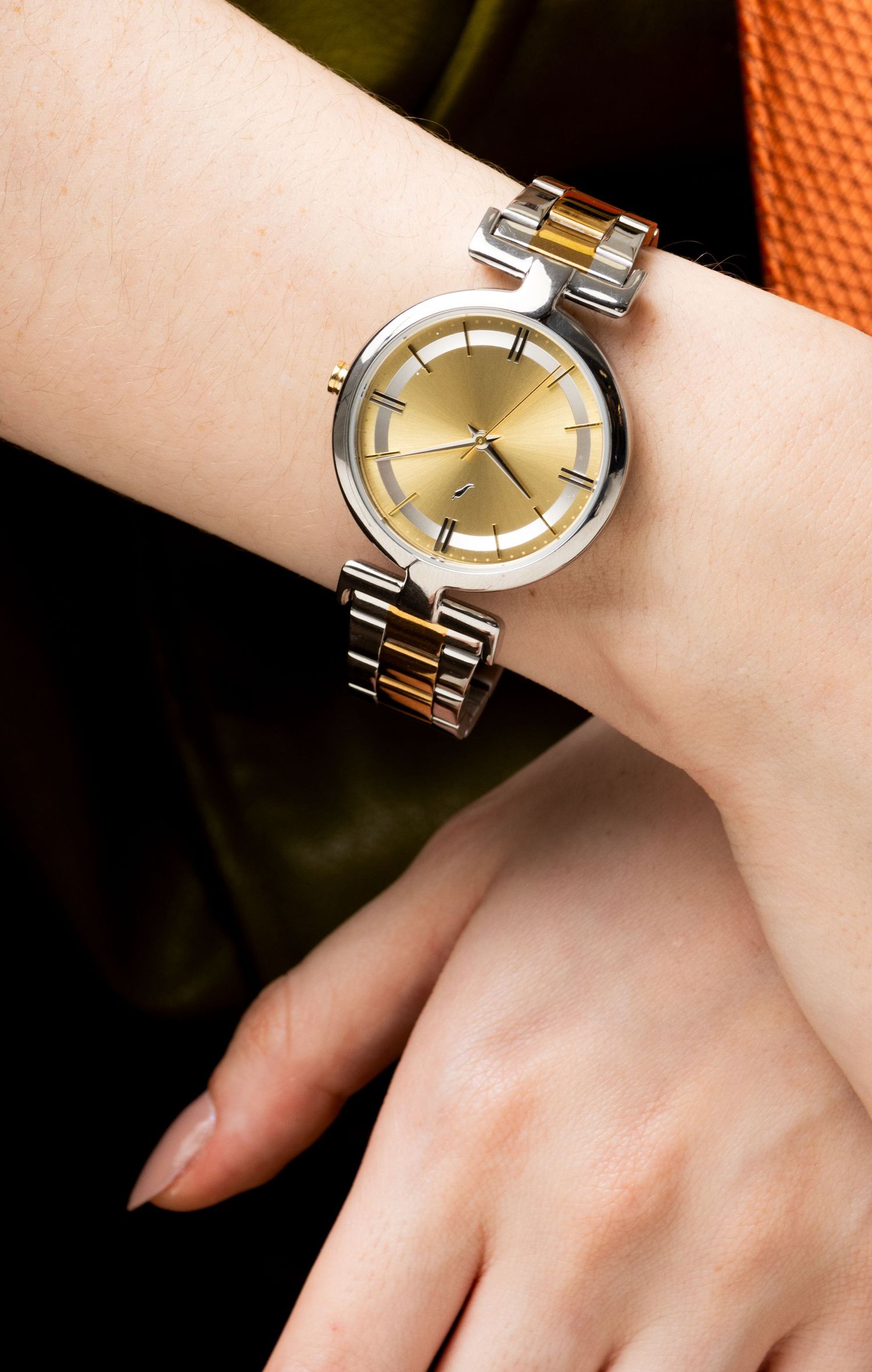 Close-up of a woman's wrist wearing a two-tone silver and gold round watch with a gold dial and a curved case design.
