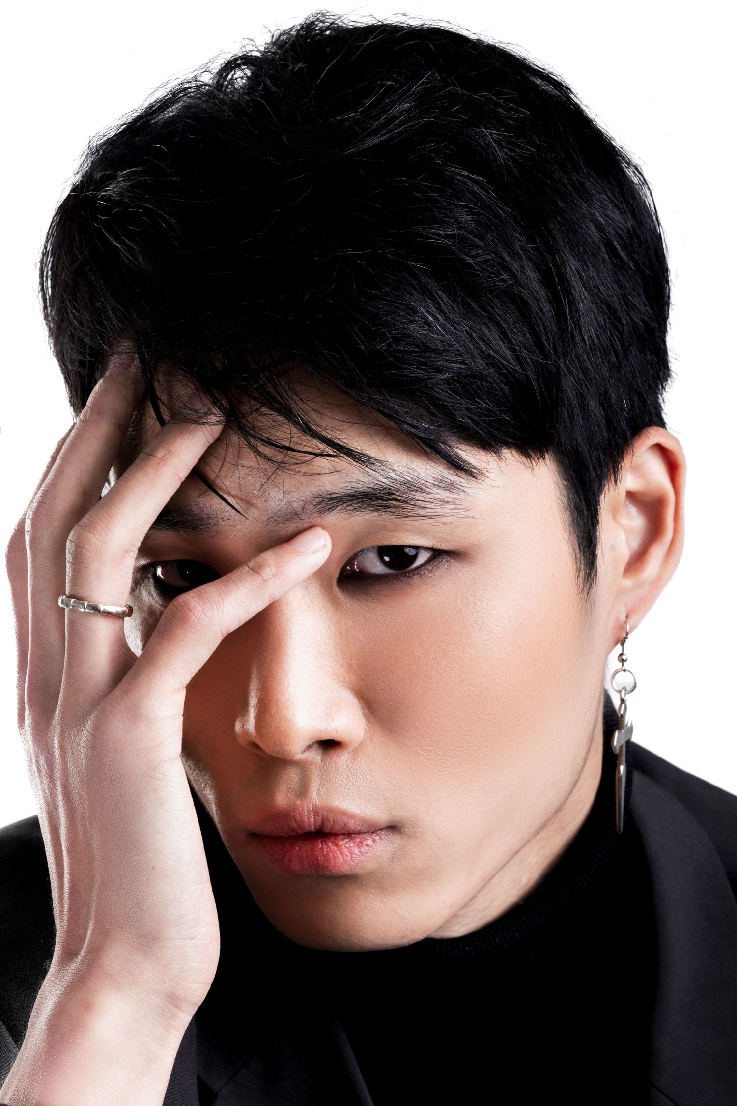 Close-up portrait of a man with dark hair covering half his face with his hand, wearing a ring and a dangling earring.