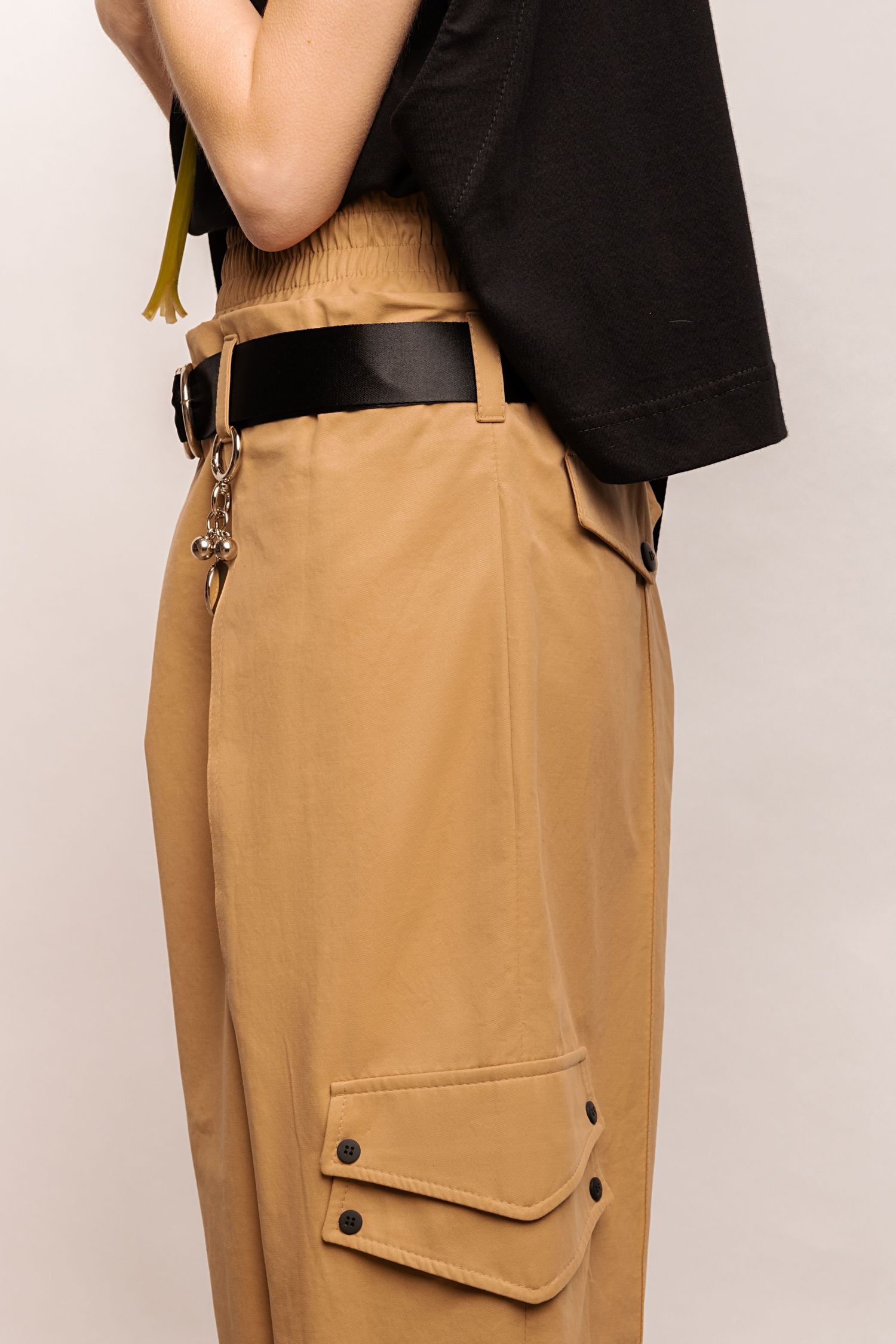 Close-up of tan cargo trousers with flap pockets and snap buttons, a black belt with chain accessories and a black cropped top.
