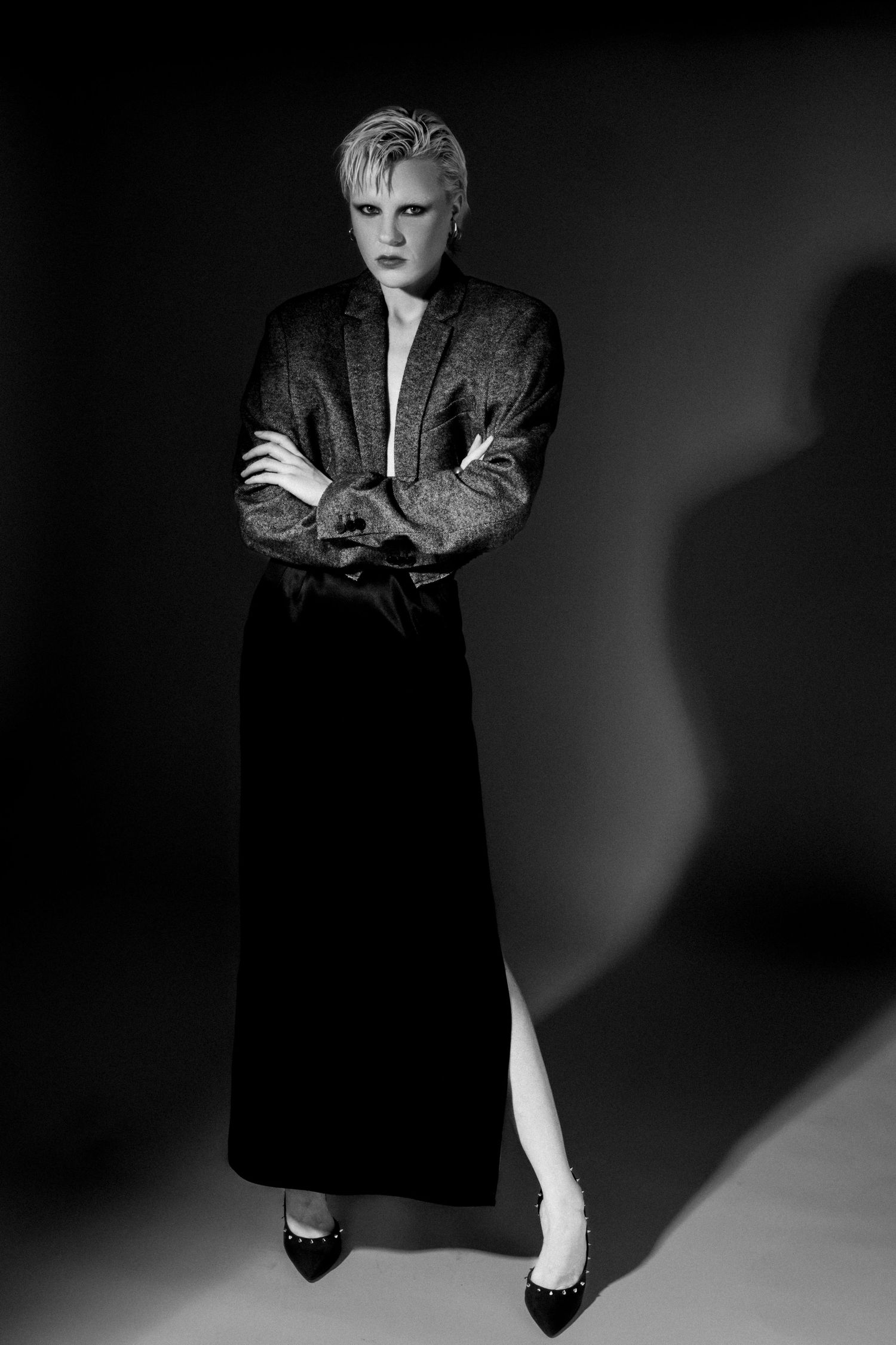 Black and white portrait of a model with short hair and crossed arms in an oversized blazer, long black skirt and pointed heels.