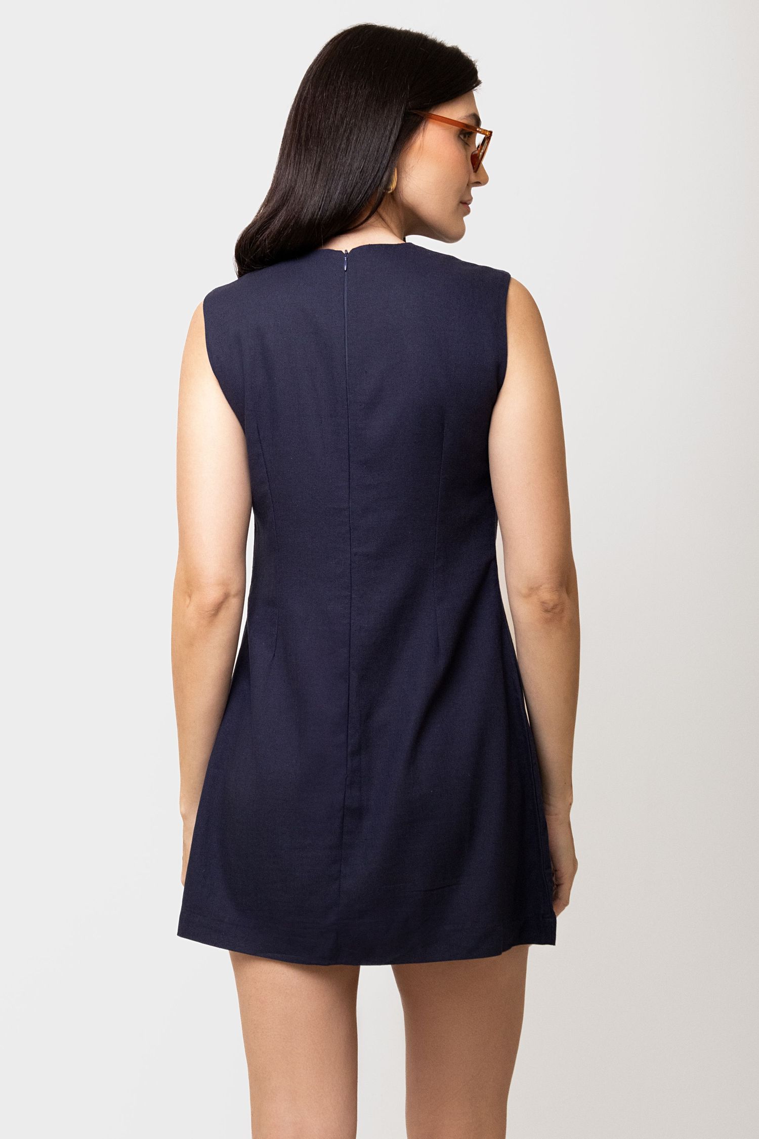 Back view of a navy sleeveless mini shift dress with a center zipper on a woman with long dark hair.