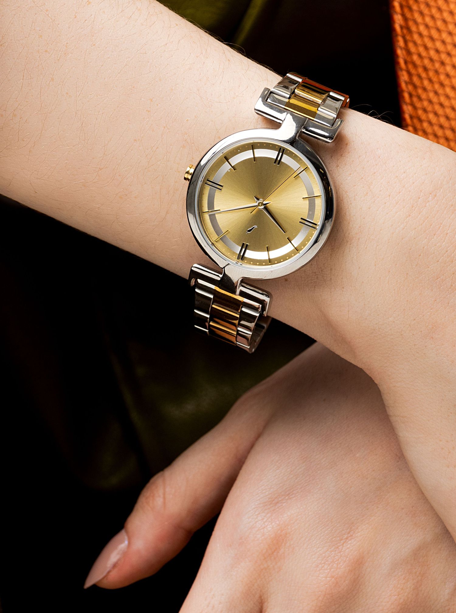 Close-up of a wrist wearing an elegant two-tone gold and silver round watch with a gold dial and a link bracelet.