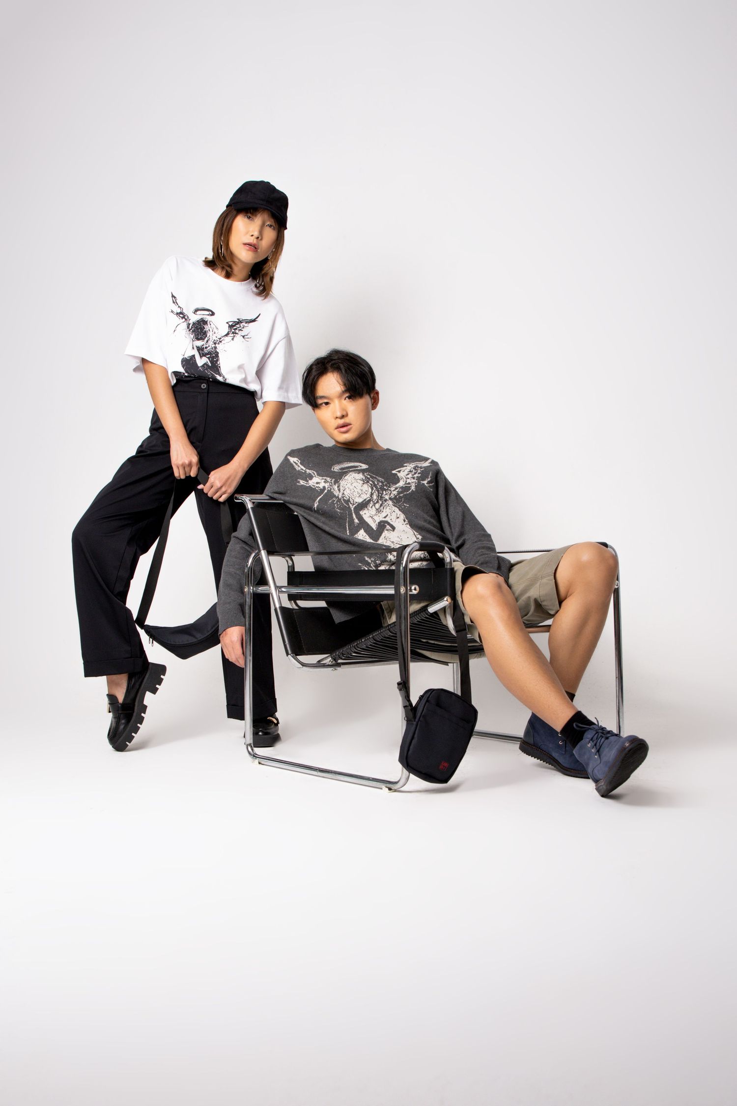 A cap-wearing model leans on a chrome chair while a seated model in a graphic sweater and shorts looks at the camera.