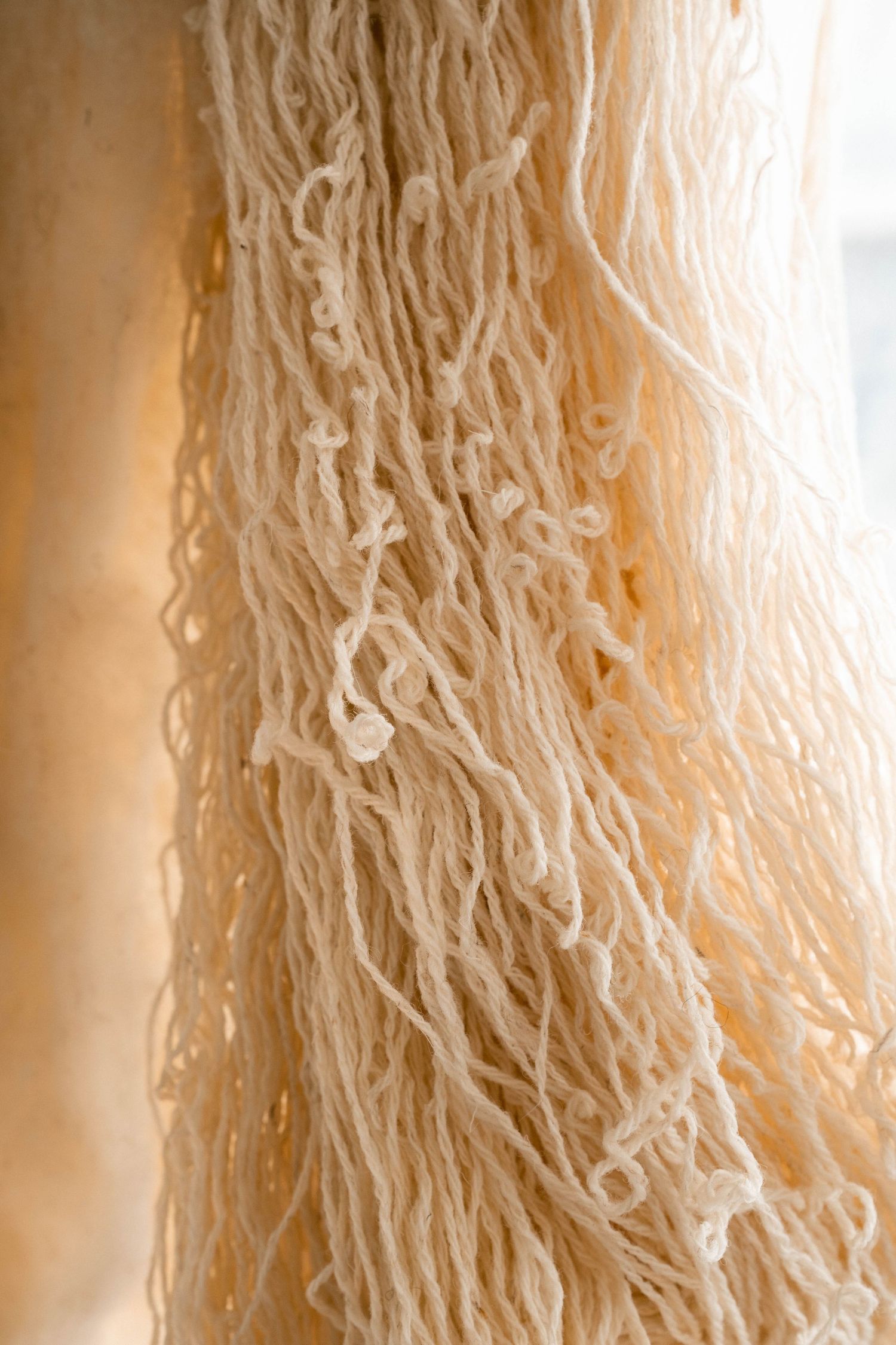 Hanging cream wool yarn strands with loose loops and natural texture in soft light.