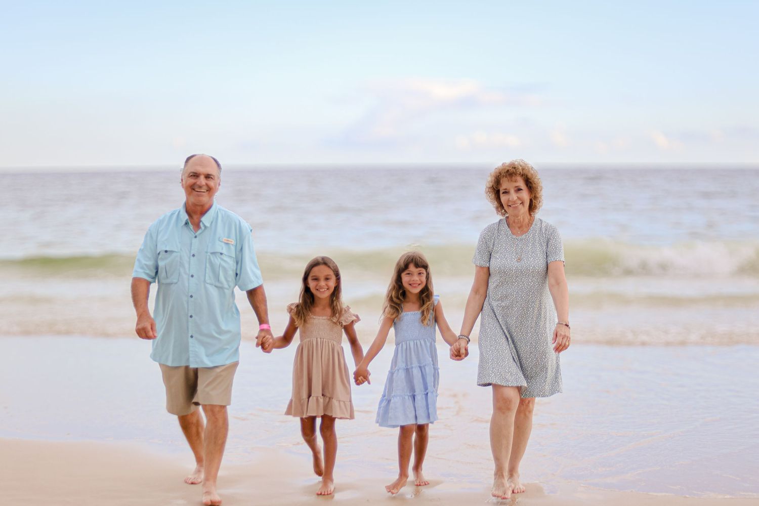 Family members holding hands while walking together on a sandy beach during golden hour.
