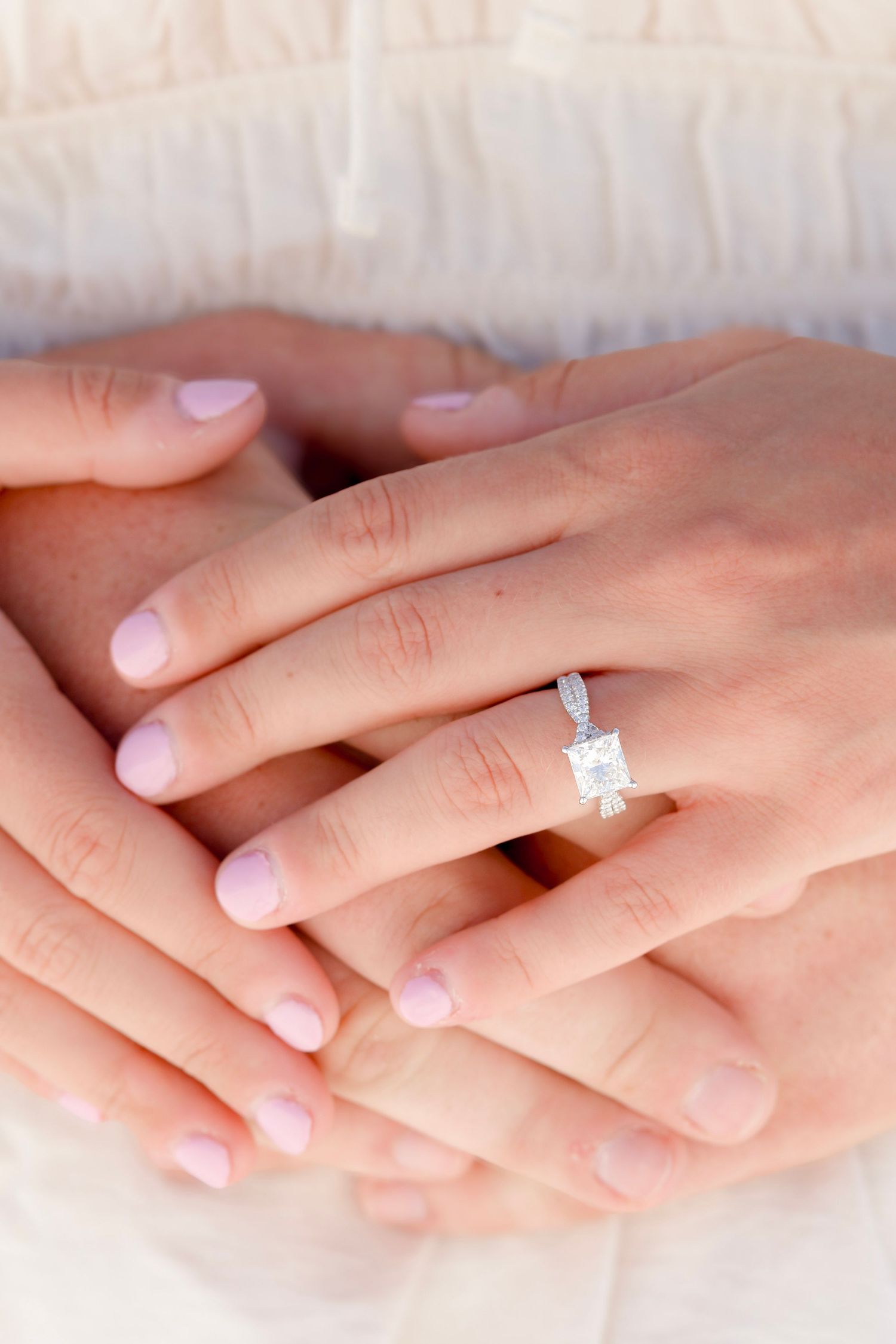 Close-up of hands with perfectly manicured nails wearing a stunning solitaire princess cut diamond engagement ring.