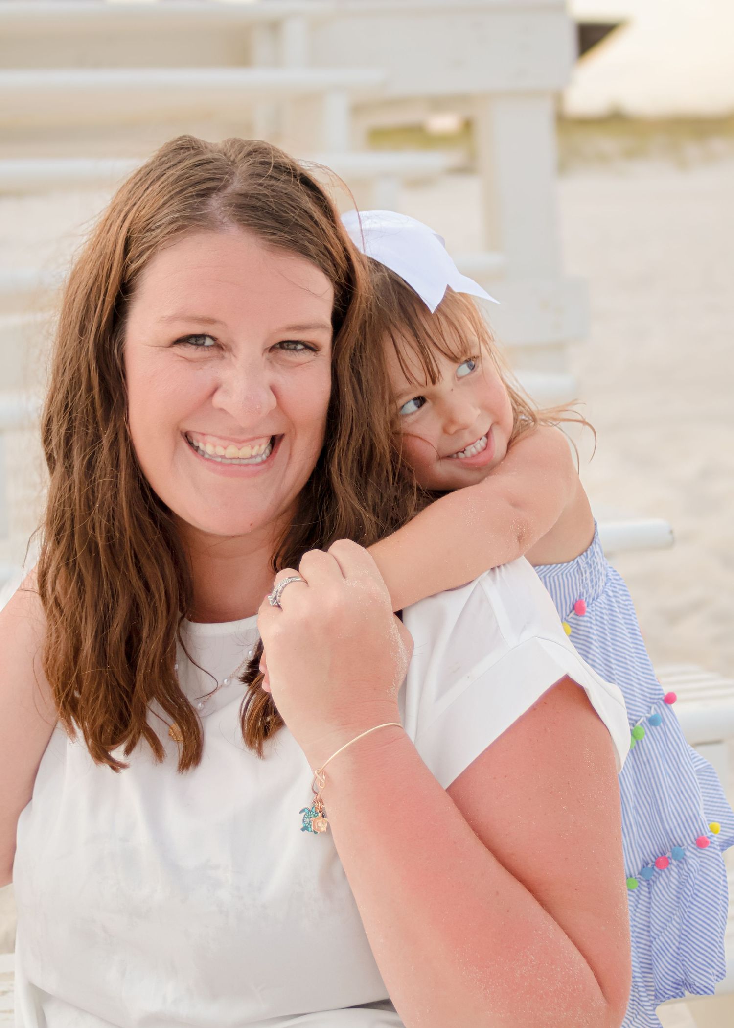 Two people in white tops share a joyful embrace at an outdoor location with light colored background.