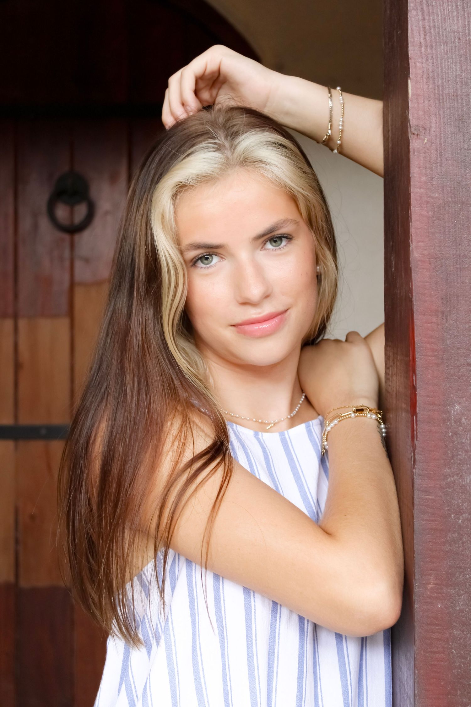 Portrait of a young woman in a striped white top leaning against a doorway.
