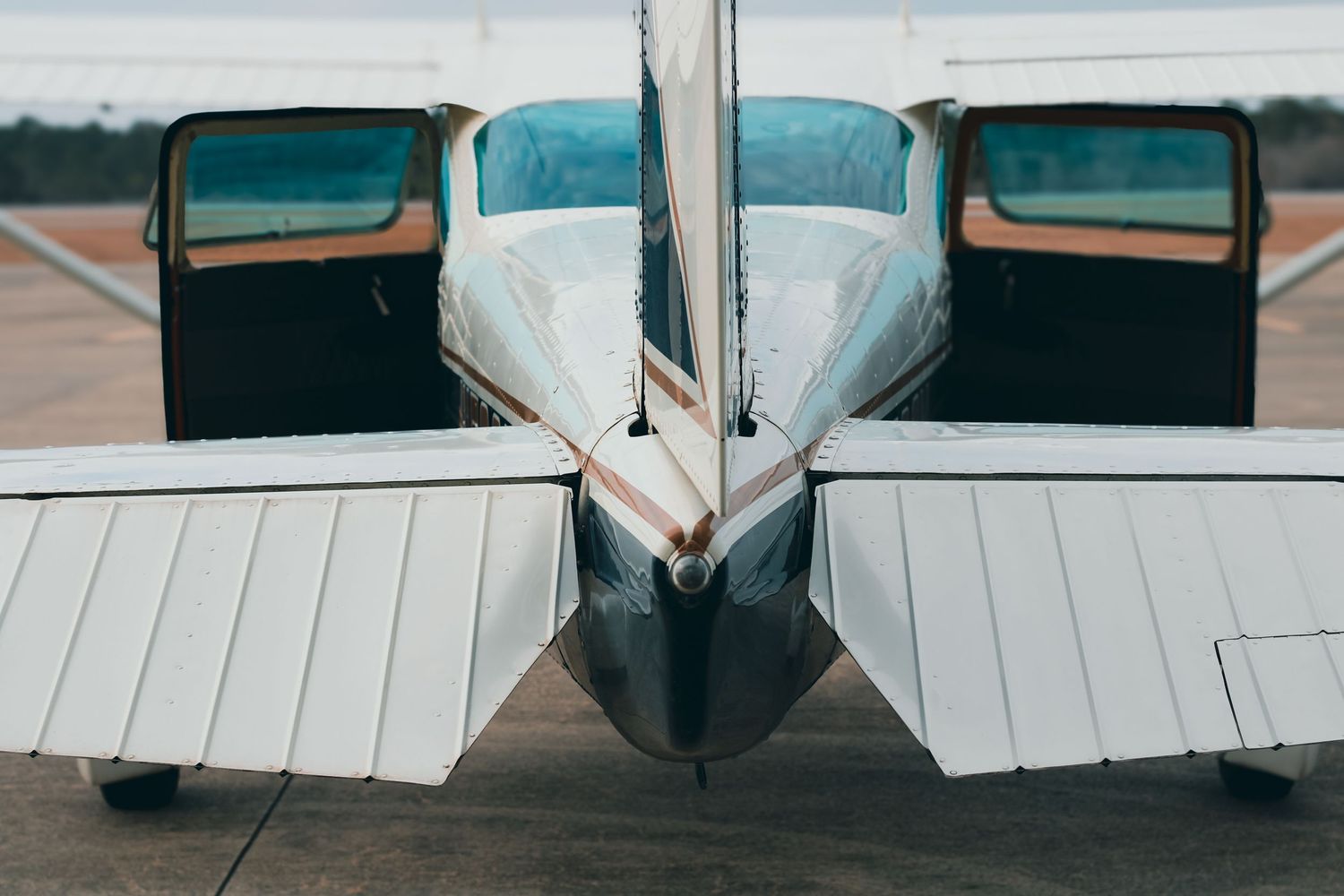 Rear view of a small aircraft showing twin engines and tail section on tarmac.